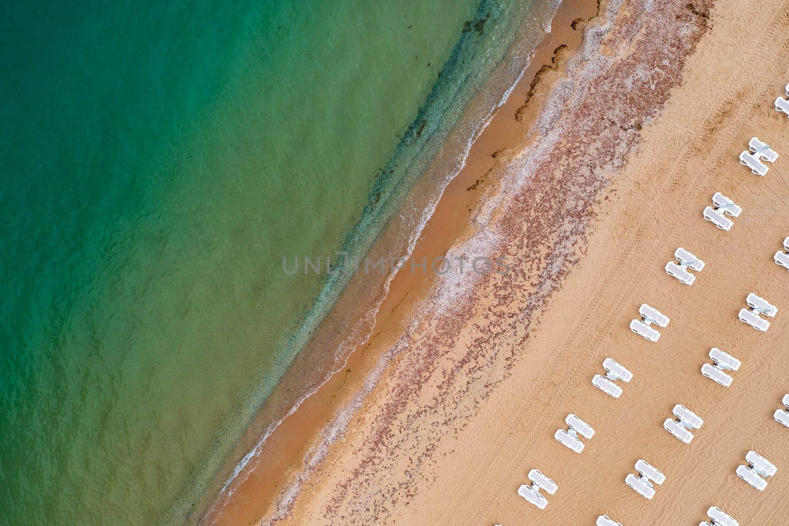 Aerial view of a beach with white sunbeds and a calm sea.