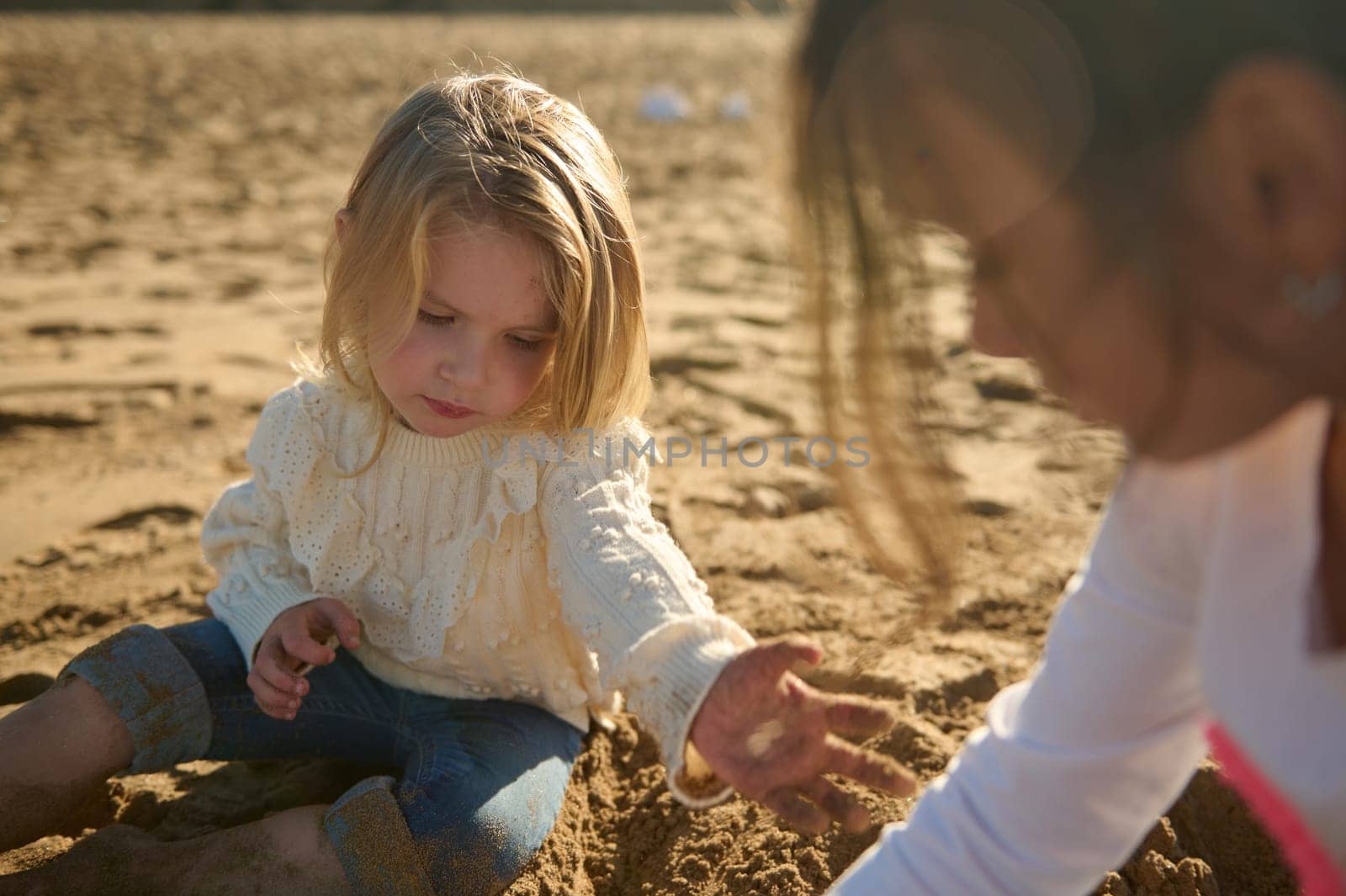 Close-up portrait of Caucasian beautiful little girls playing with sand on the beach by artgf