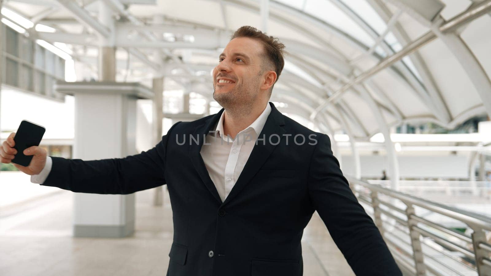 Skilled businessman receive good news for getting promotion while walking at corridor. Happy smart manager calling or talking to telephone with marketing team for increasing sales. Lifestyle. Urbane.