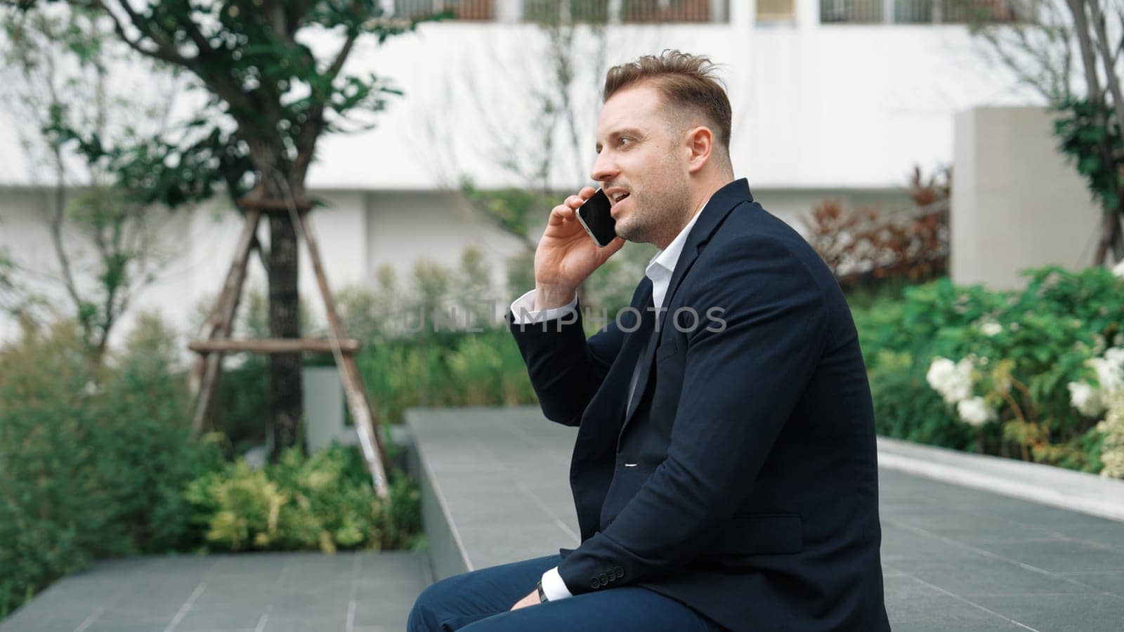 Side view of businessman sitting at park while talking to investors about marketing strategy. Caucasian executive manager looking increasing sales or successful project at eco city. Lifestyle. Urbane