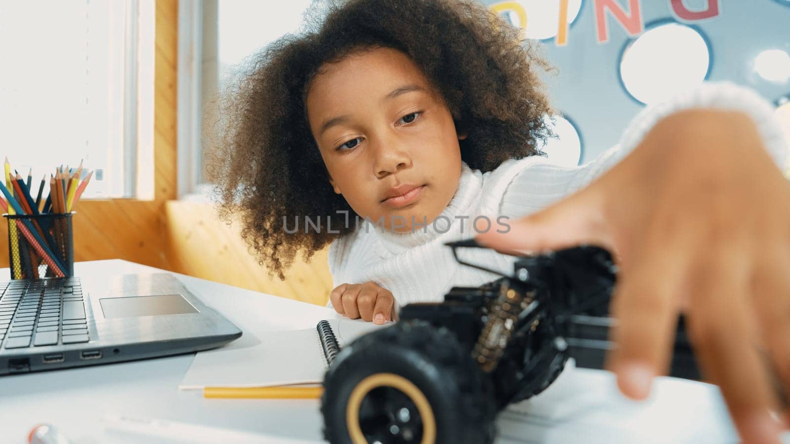 Smart african girl build robotic car while using wires while using laptop setting or writing prompt code. Skilled female student working on computer in STEM technology online classroom. Erudition.