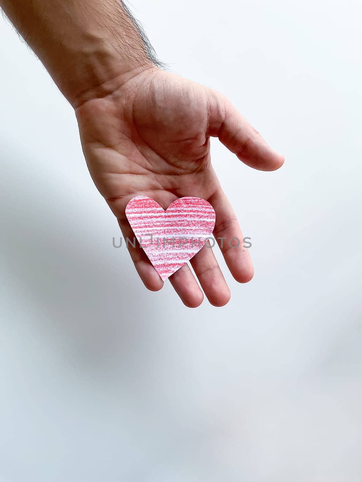Mans hand holding striped pink paper heart against white background, symbolizing love and care, with copy space. Can be used for design and print related to childrens, love and relationships themes, charity and healthcare campaigns, emotional and mental well being content. High quality photo