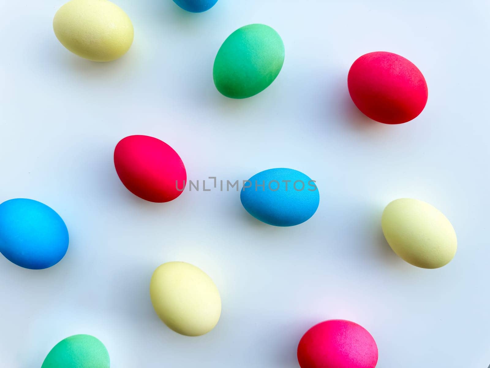 Colorful Easter eggs scattered on white background, flat lay composition for spring holiday celebration and decoration ideas. For Easter holiday promotions, themed party invitations, seasonal blog posts, educational materials about Easter, background imagery for websites and social media platforms celebrating the spring season. by Lunnica