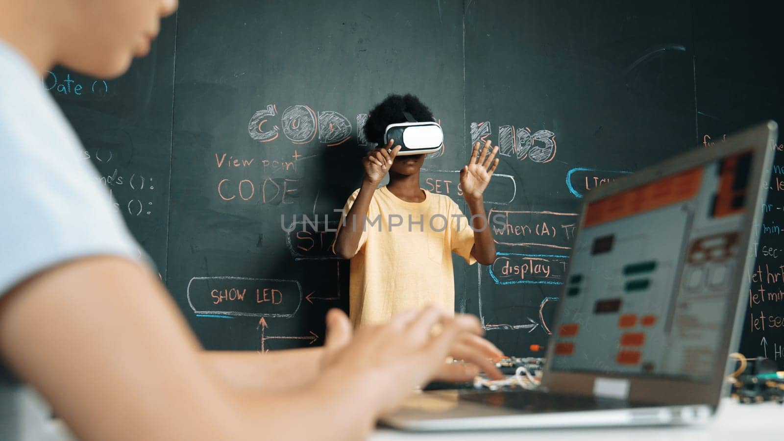 Closeup of school girl hand coding program while african student using VR interact with metaworld. Smart boy wearing virtual reality glasses and playing video games at innovative class. Edification.