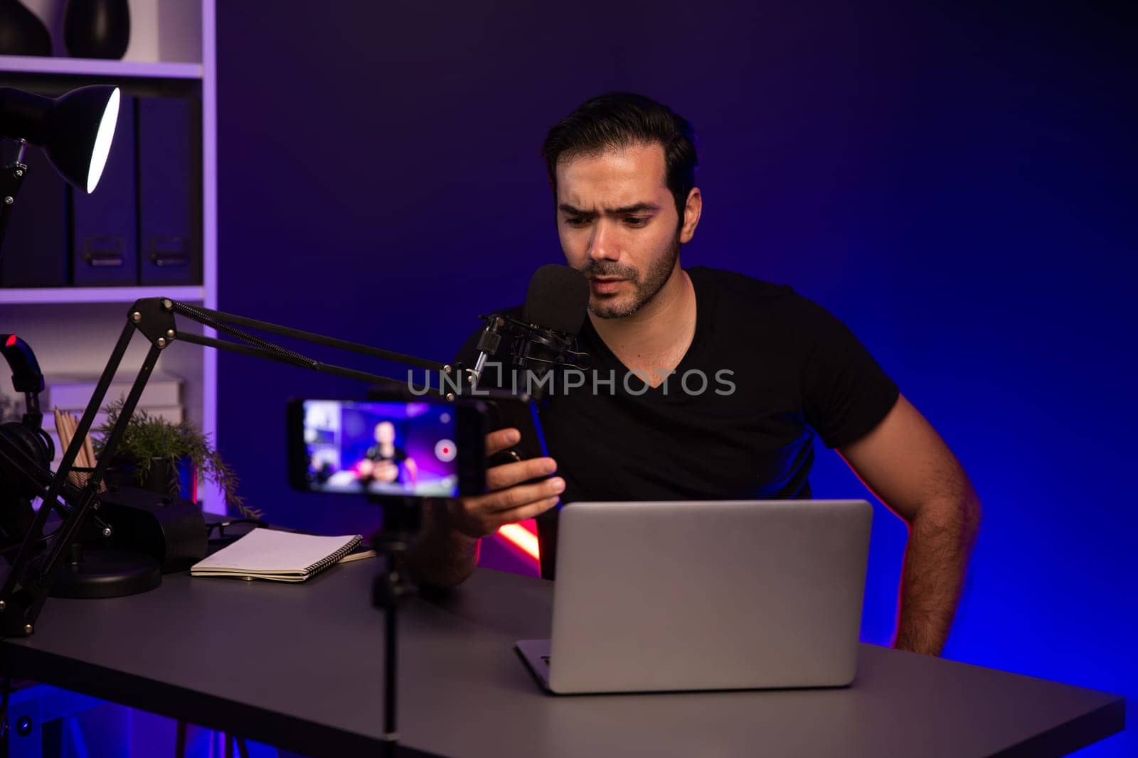 Broadcaster talking to listener on live streaming online with blurred screen, reading comment on smartphone on social media channel by creative positive thinking at purple neon light studio. Surmise.