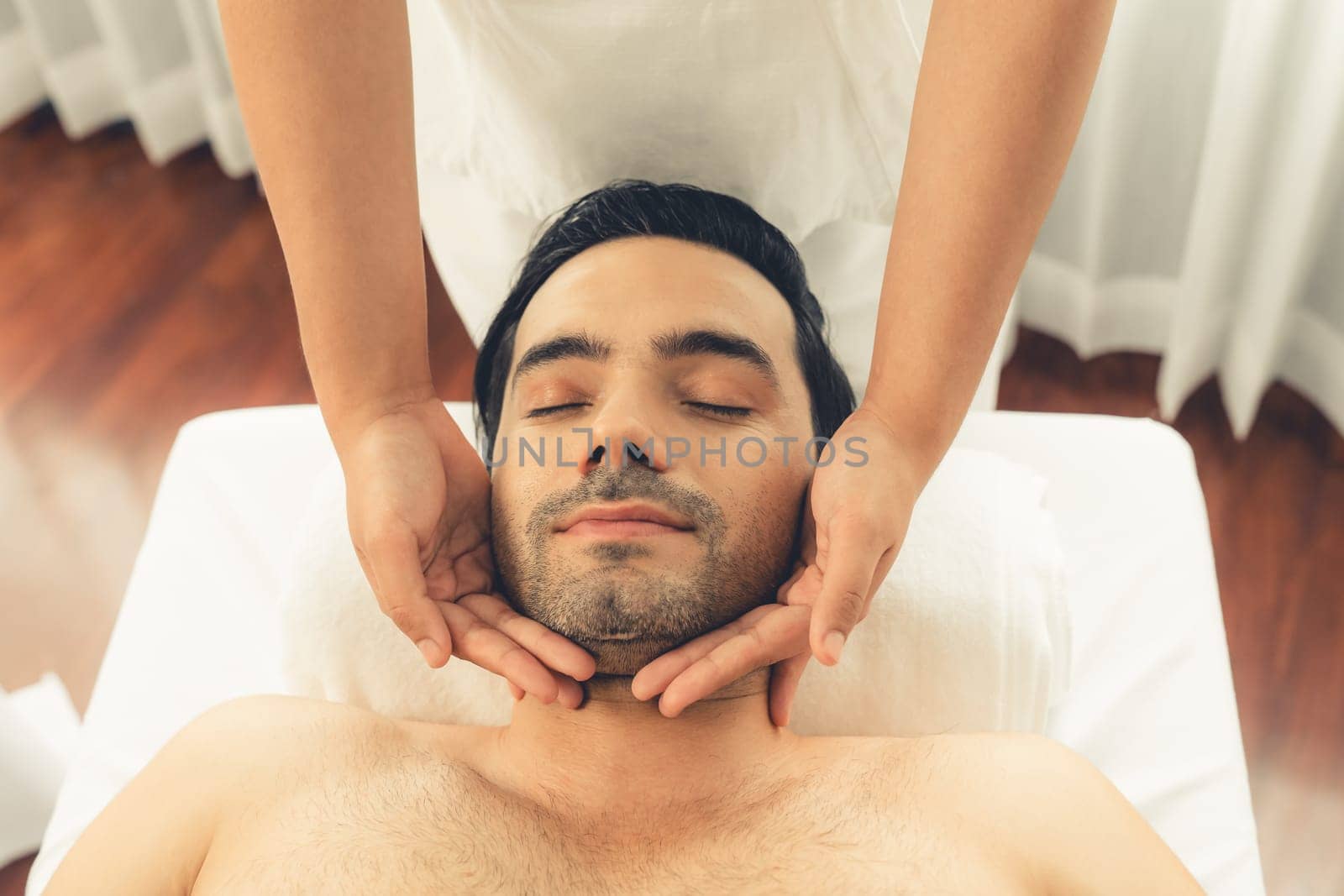 Caucasian man enjoying relaxing anti-stress head massage and pampering facial beauty skin recreation leisure in dayspa modern light ambient at luxury resort or hotel spa salon. Quiescent