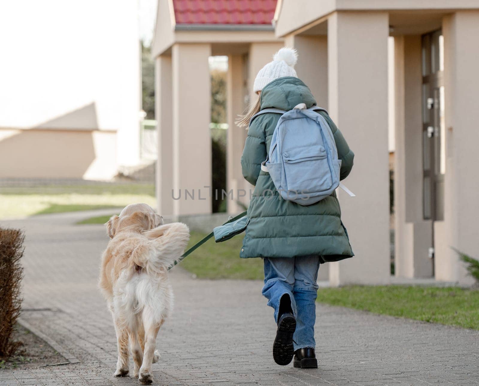 Girl With Golden Retriever Strolls Down Street In Early Spring, Viewed From Behind