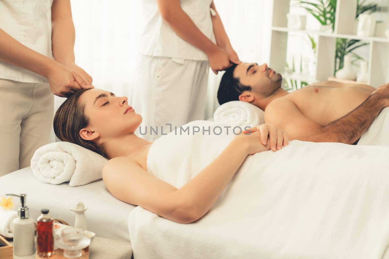 Caucasian couple enjoying relaxing anti-stress head massage and pampering facial beauty skin recreation leisure in dayspa modern light ambient at luxury resort or hotel spa salon. Quiescent