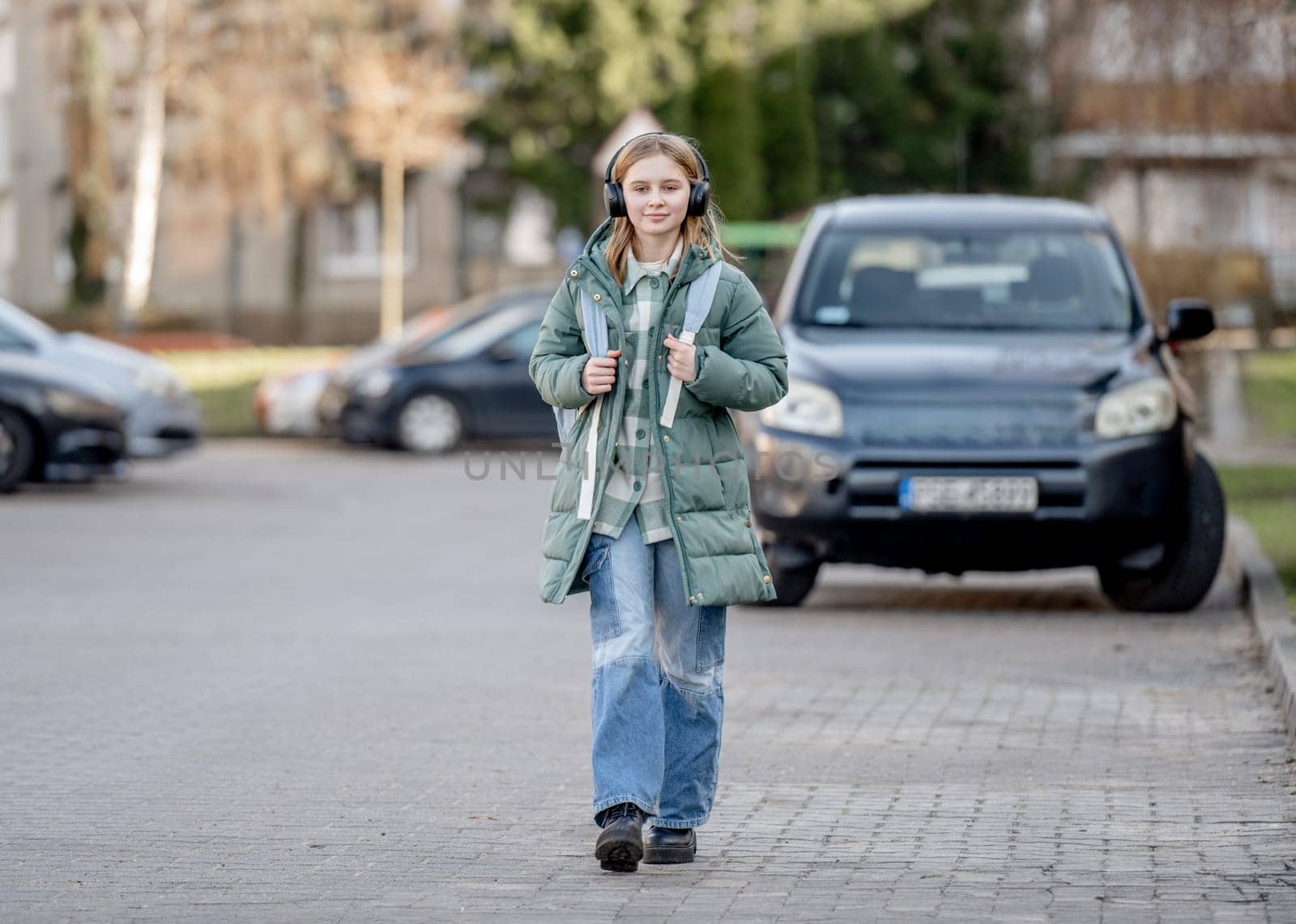 Cute Girl Walks Down Street In Spring, Listening To Music In Headphones by tan4ikk1