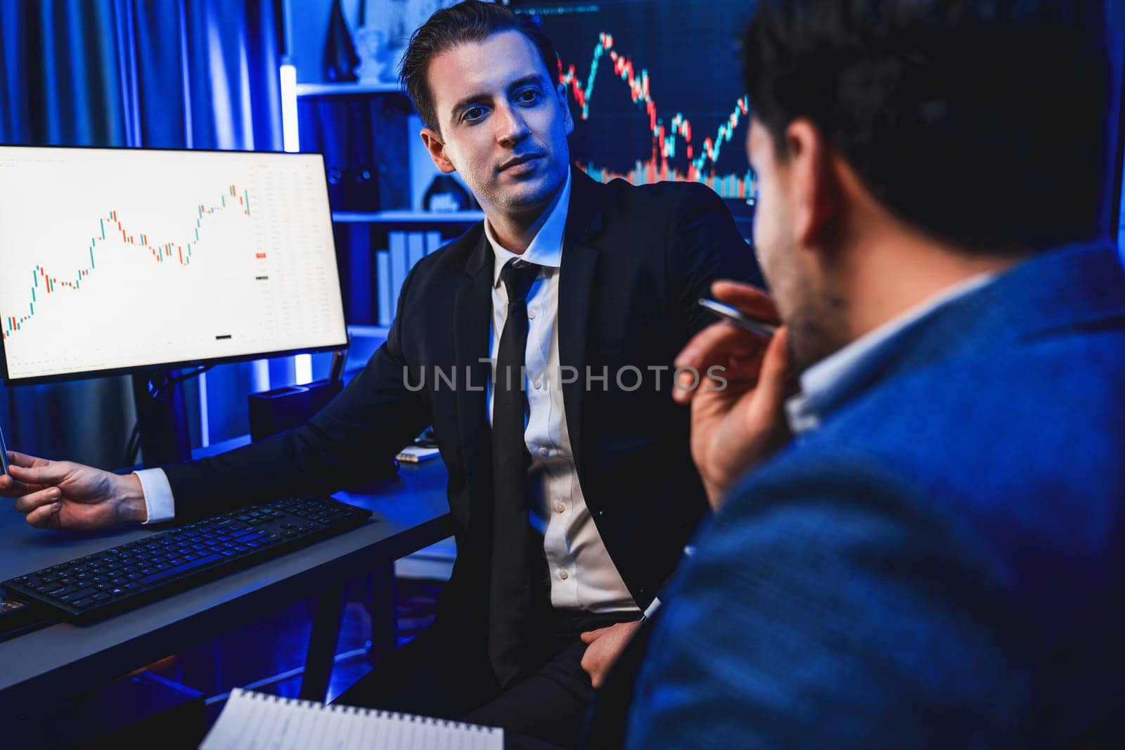 Two stock exchange traders discussing on dynamic investment graph, trending of high profit in currency stock. Showing financial benefit data on monitor screen in neon light at workplace. Sellable.