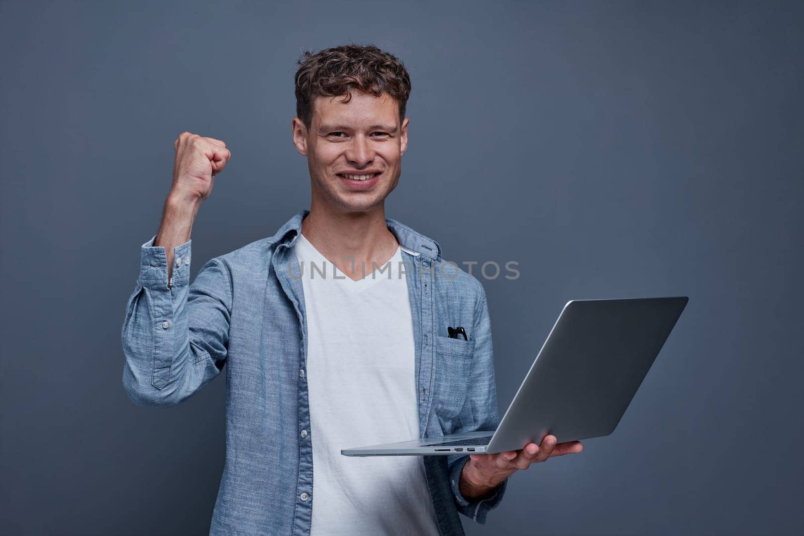 young man on gray background holding a laptop.