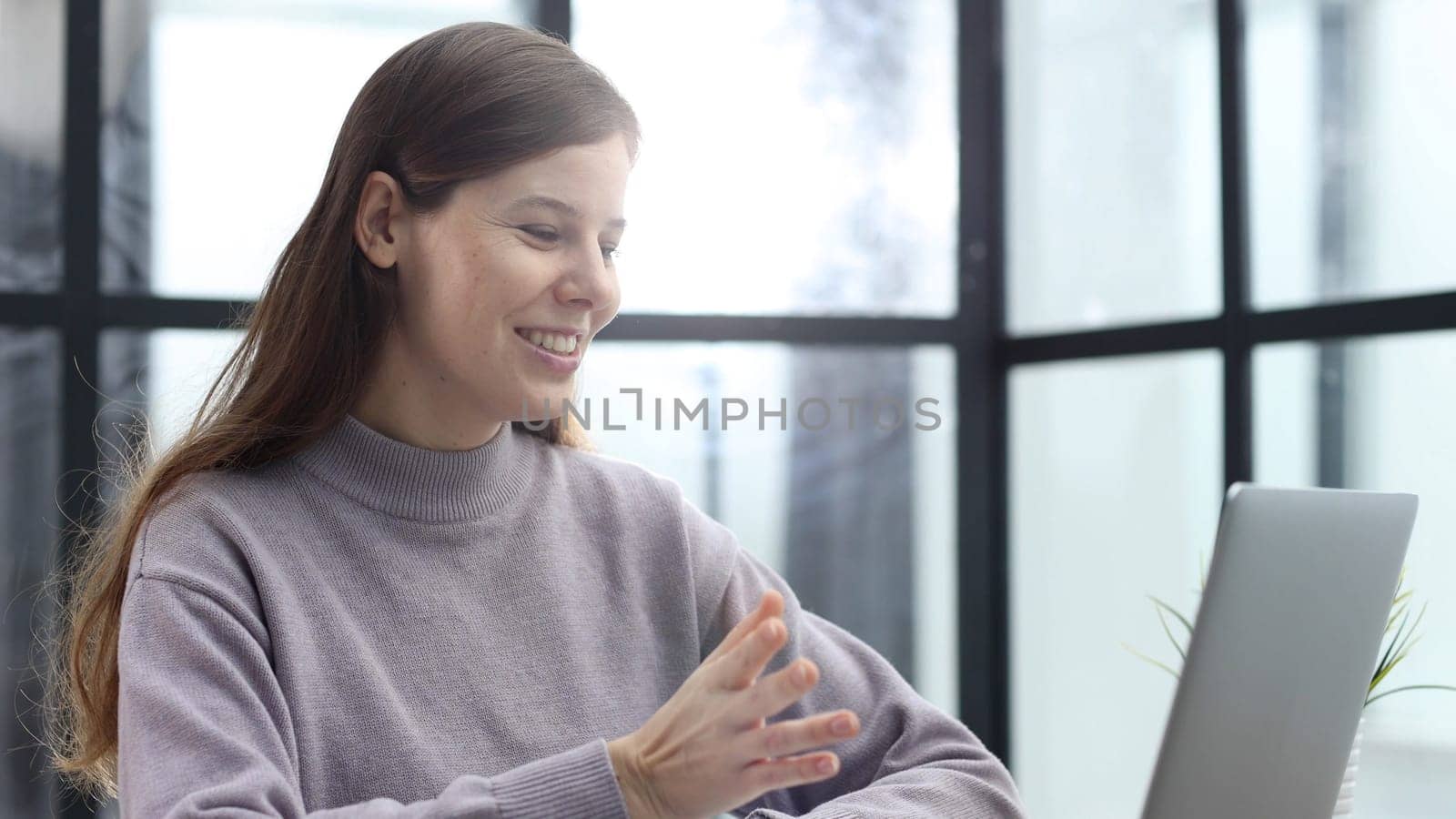 A woman in close-up at a desk in the office talking at an online video conference.