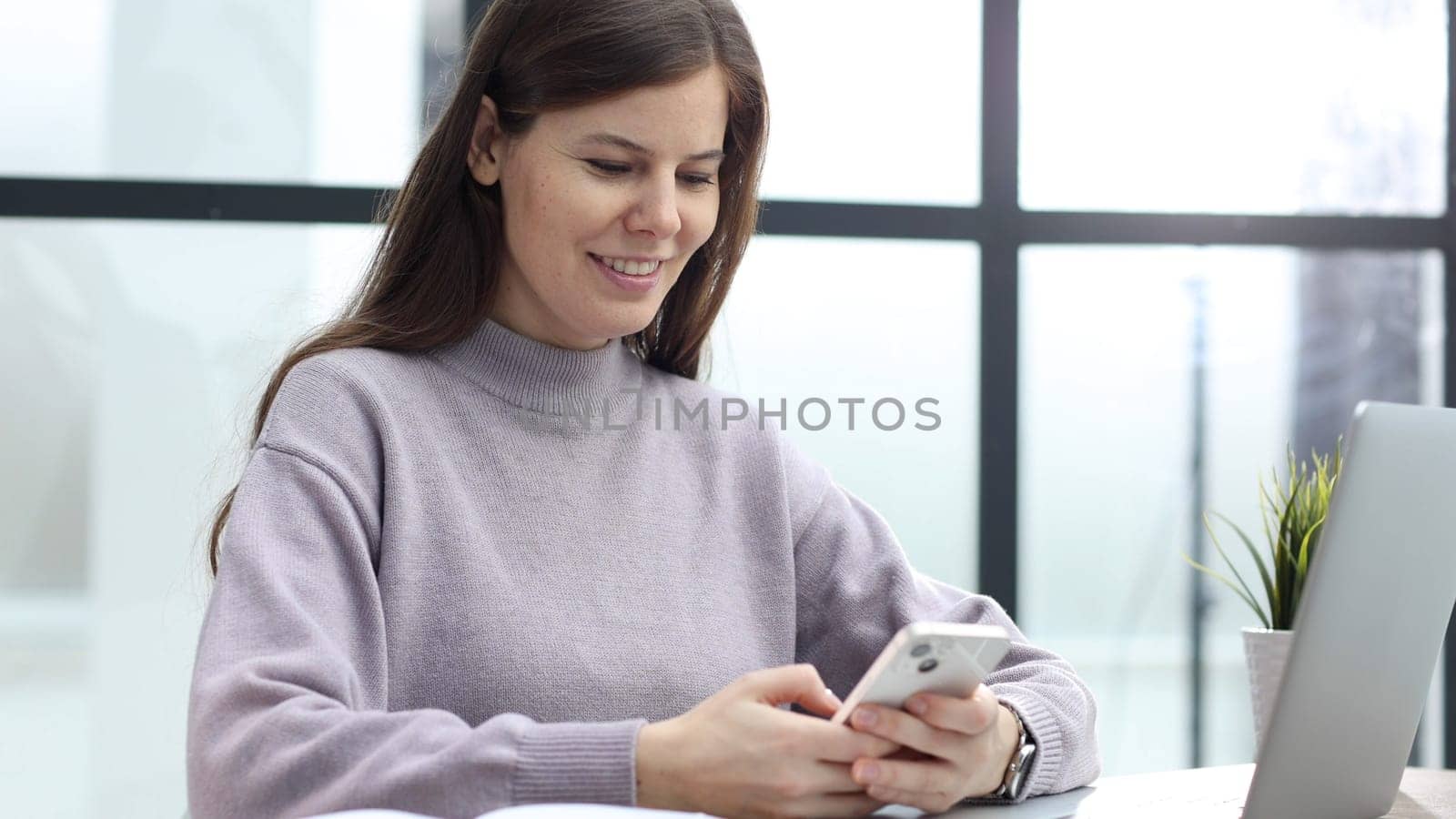 A woman in close-up at a desk in the office uses the phone for a successful transaction.