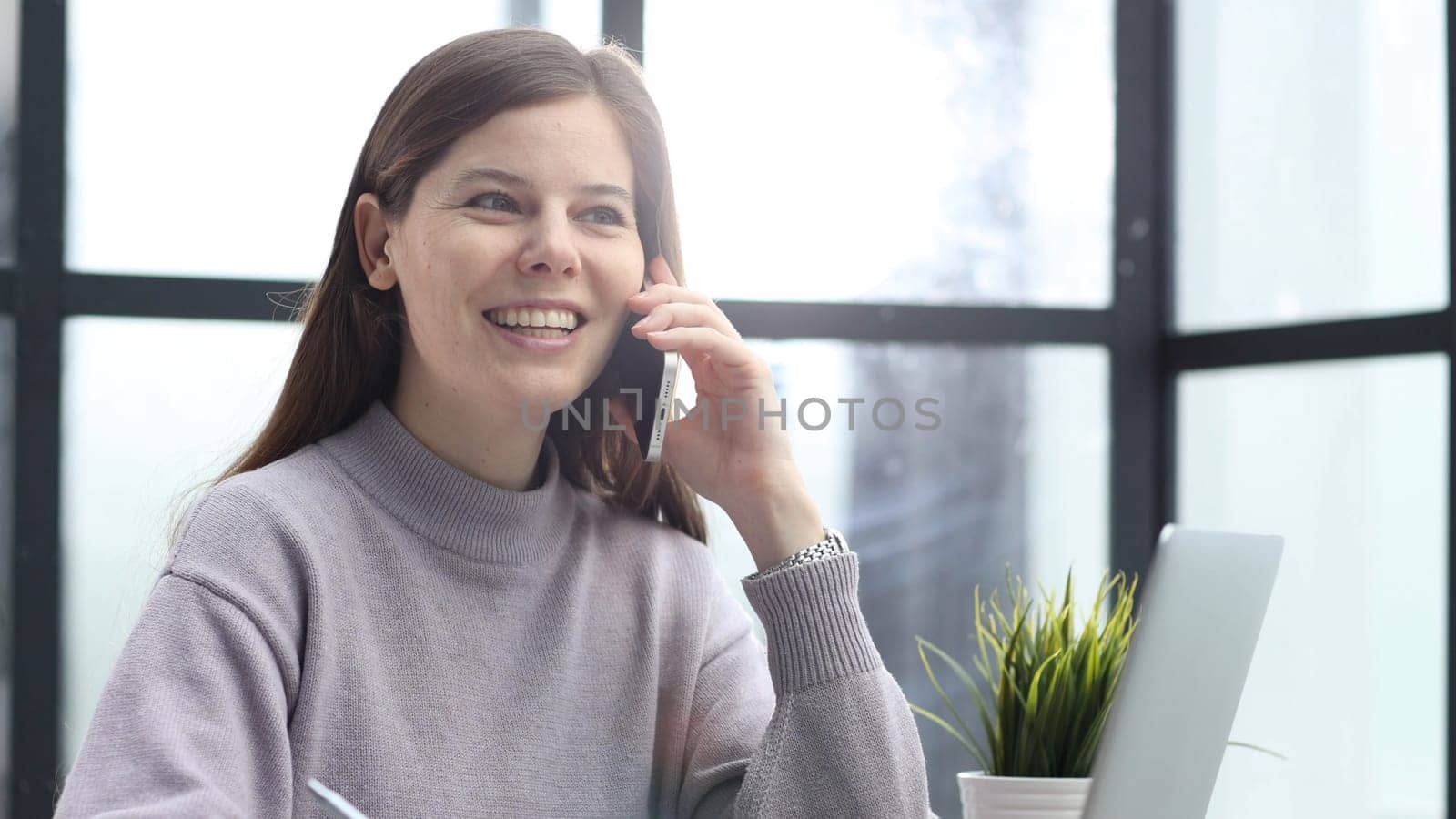 A woman in close-up at a desk in the office talking on the phone and discussing a deal.