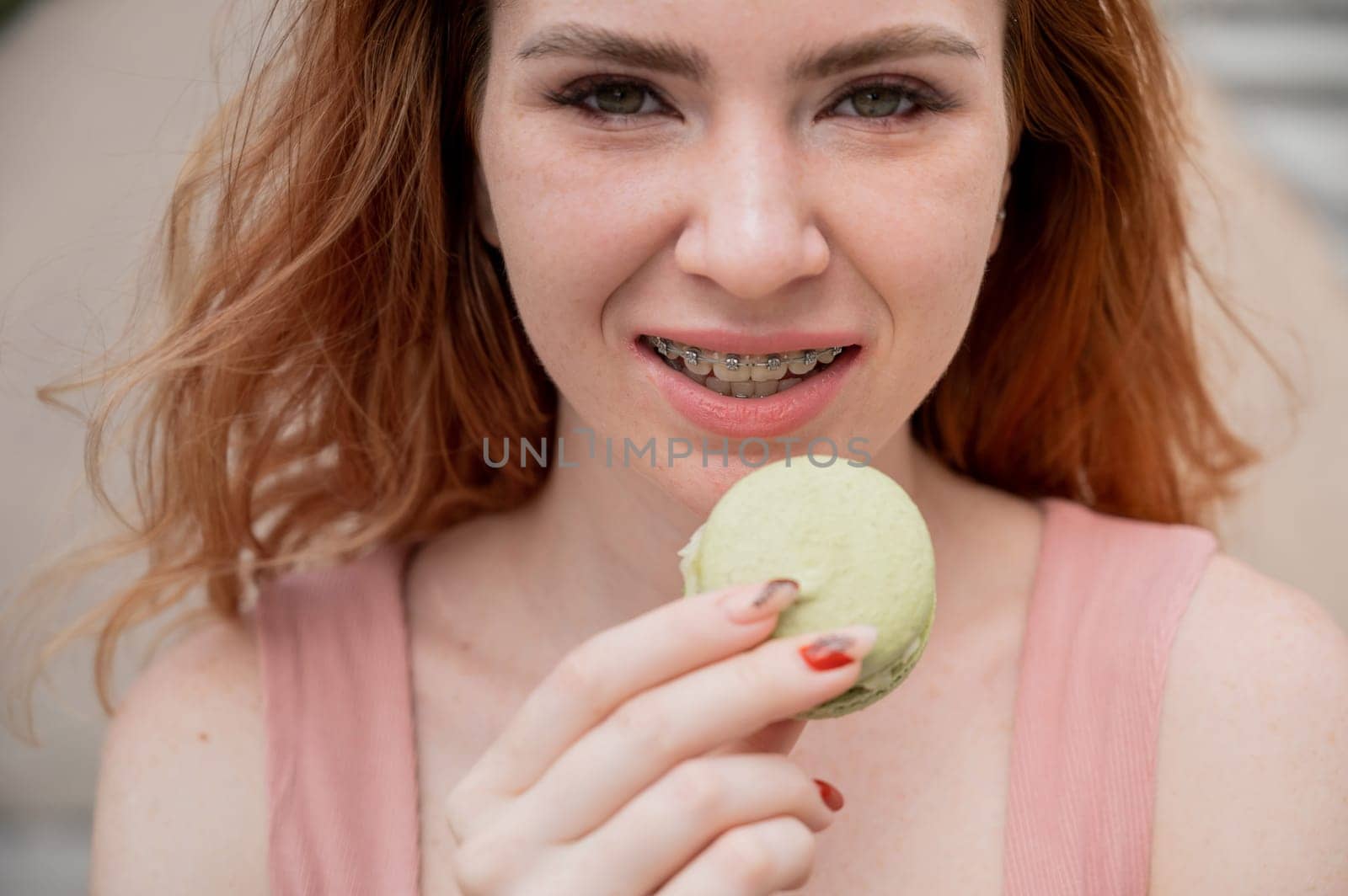 Young red-haired woman with braces eating macaron cake. by mrwed54