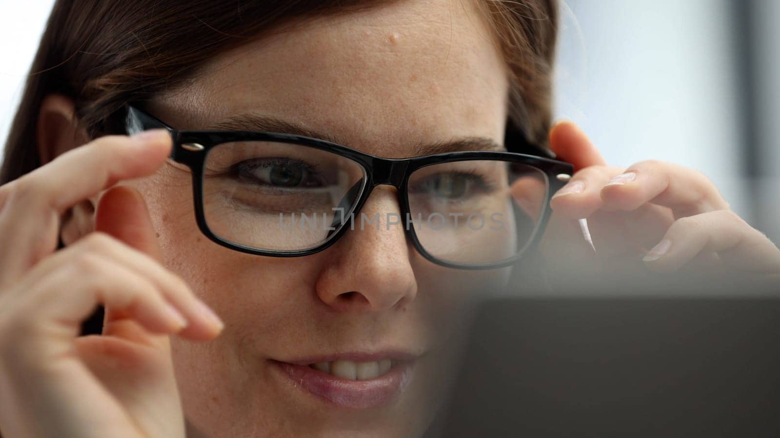 A woman's face is in close-up in the office, she is working on a laptop.
