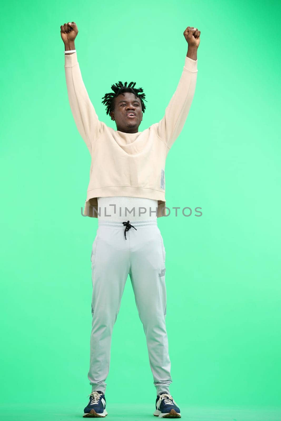 A man, full-length, on a green background, raised his hands up.