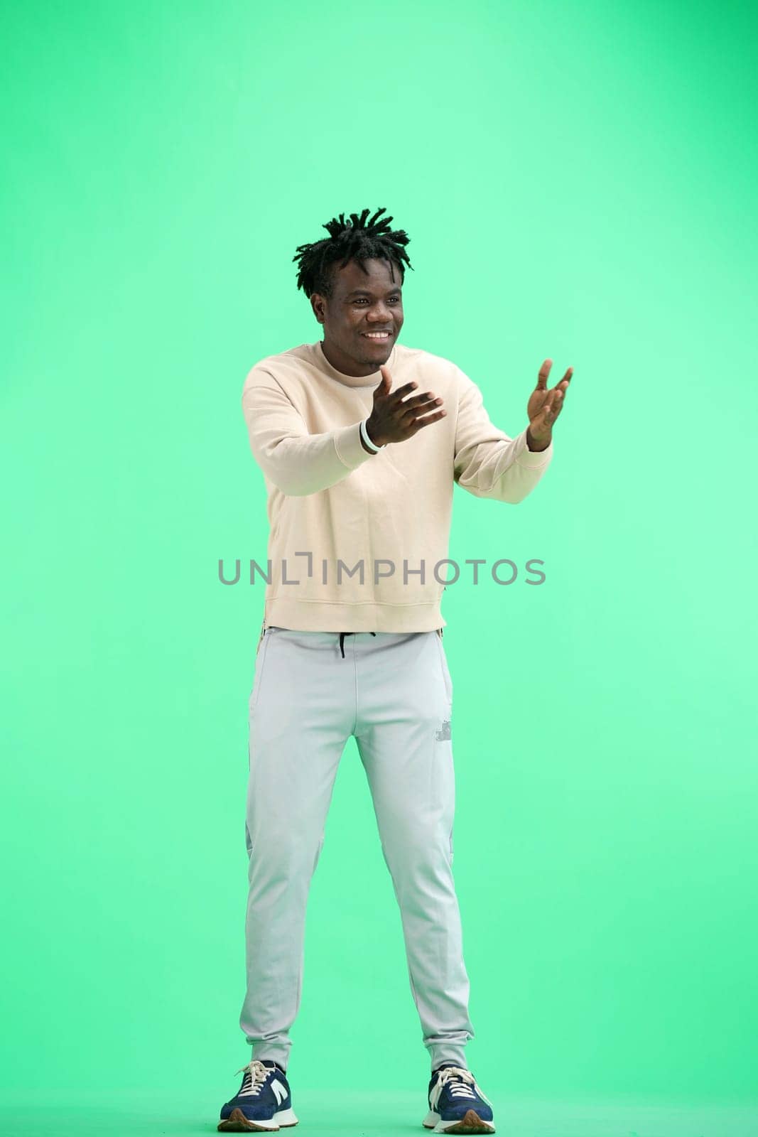 A man, full-length, on a green background, spreads his arms.