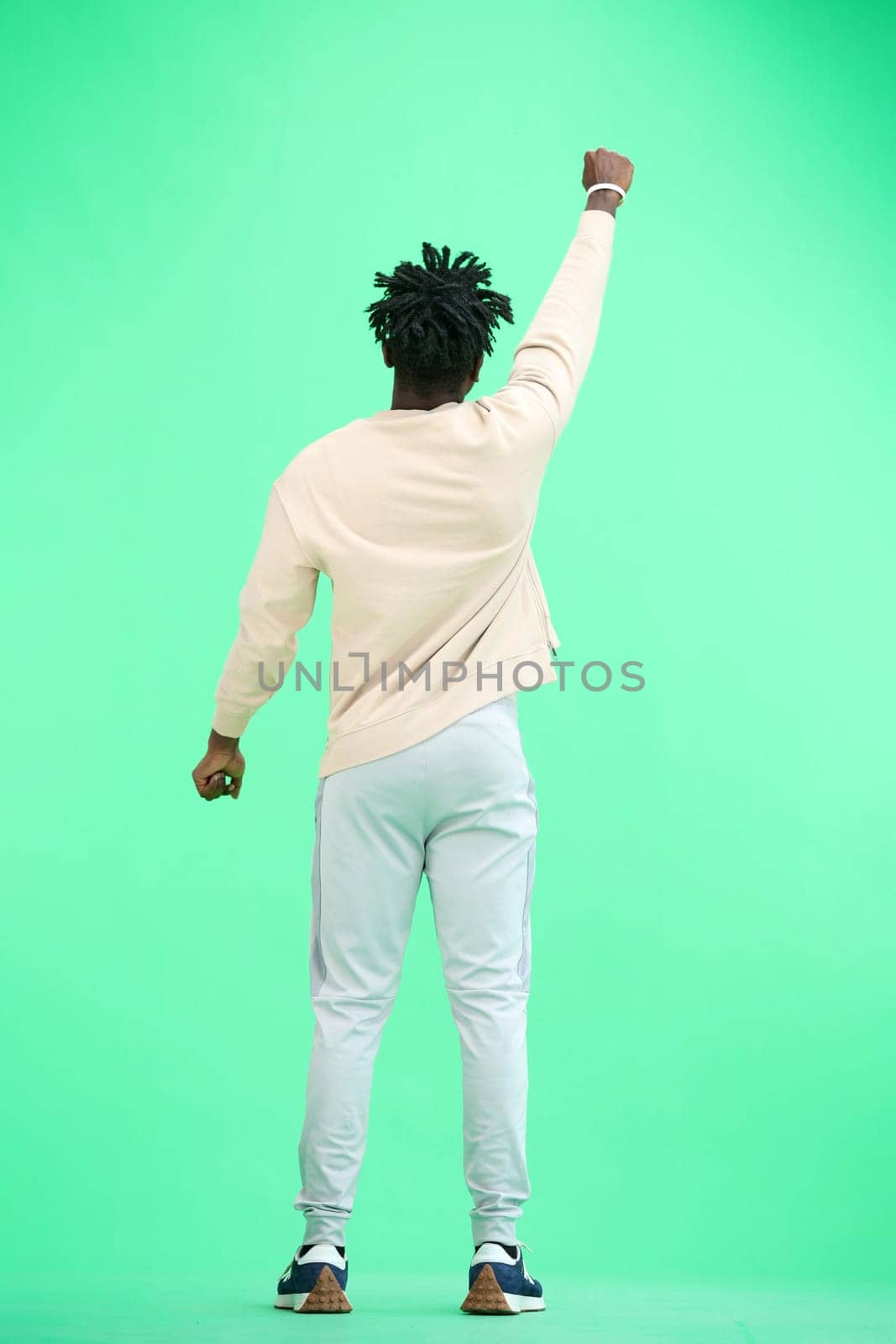 A man, full-length, on a green background, raised his hand up.
