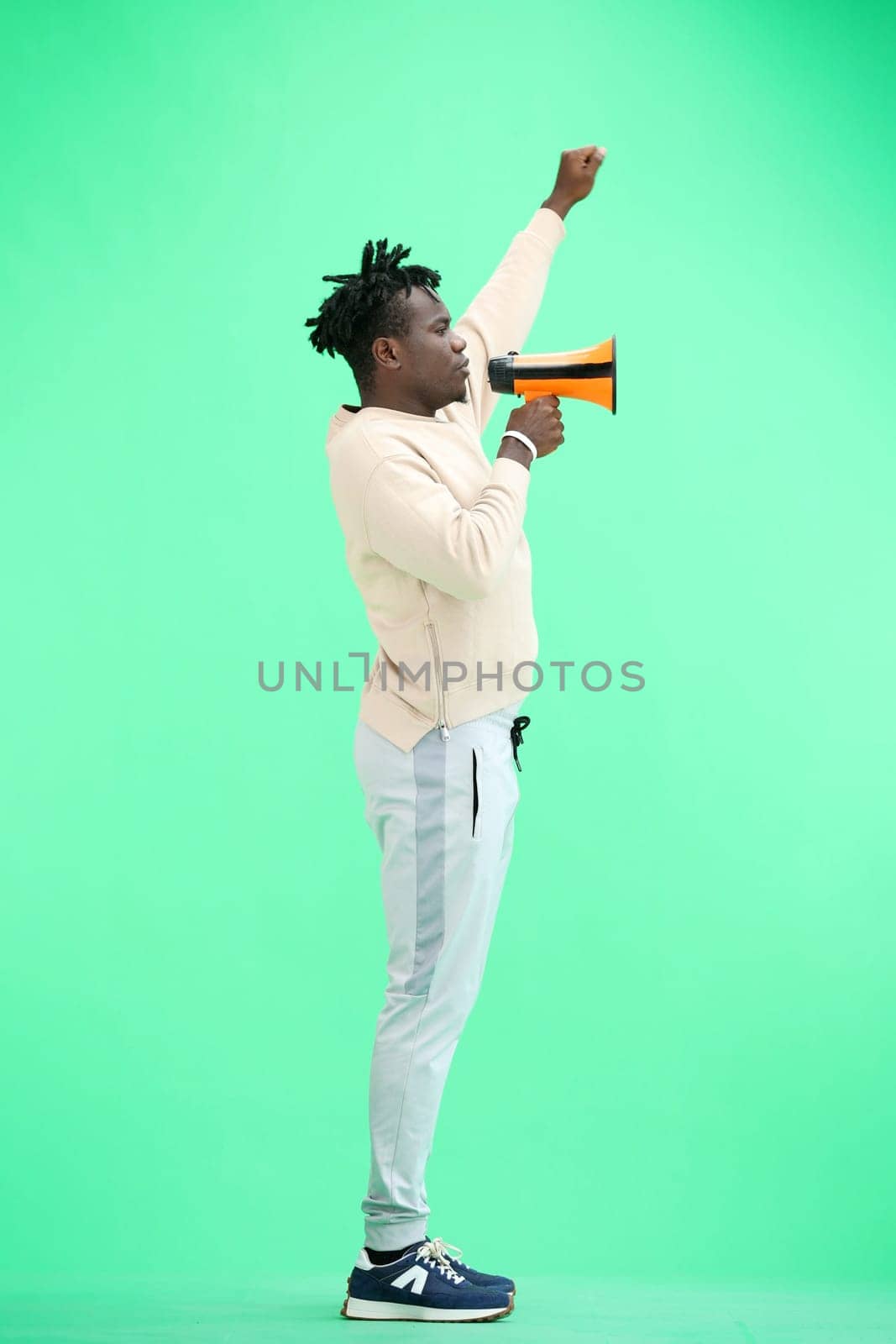 A man, full-length, on a green background, with a megaphone.