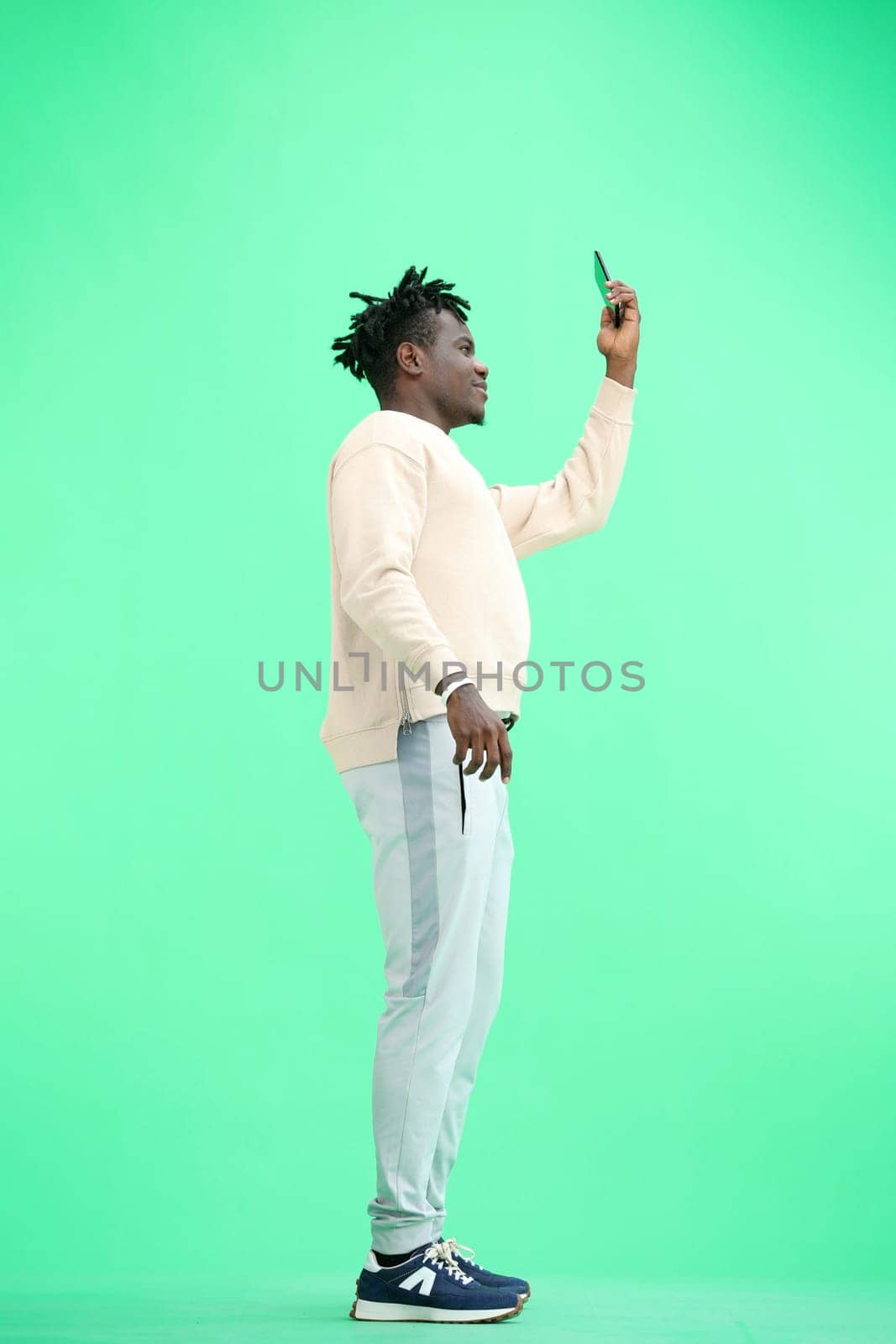 A man, full-length, on a green background, waving his phone.