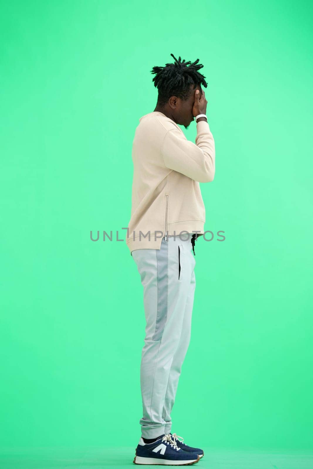A man, full-length, on a green background, facepalm.
