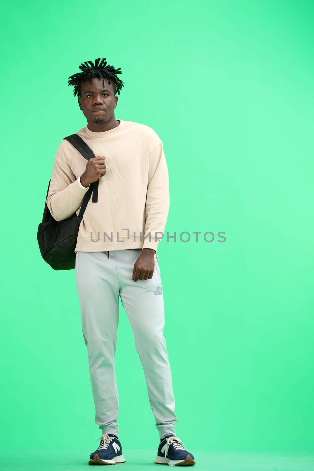 A man, full-length, on a green background, with a backpack.
