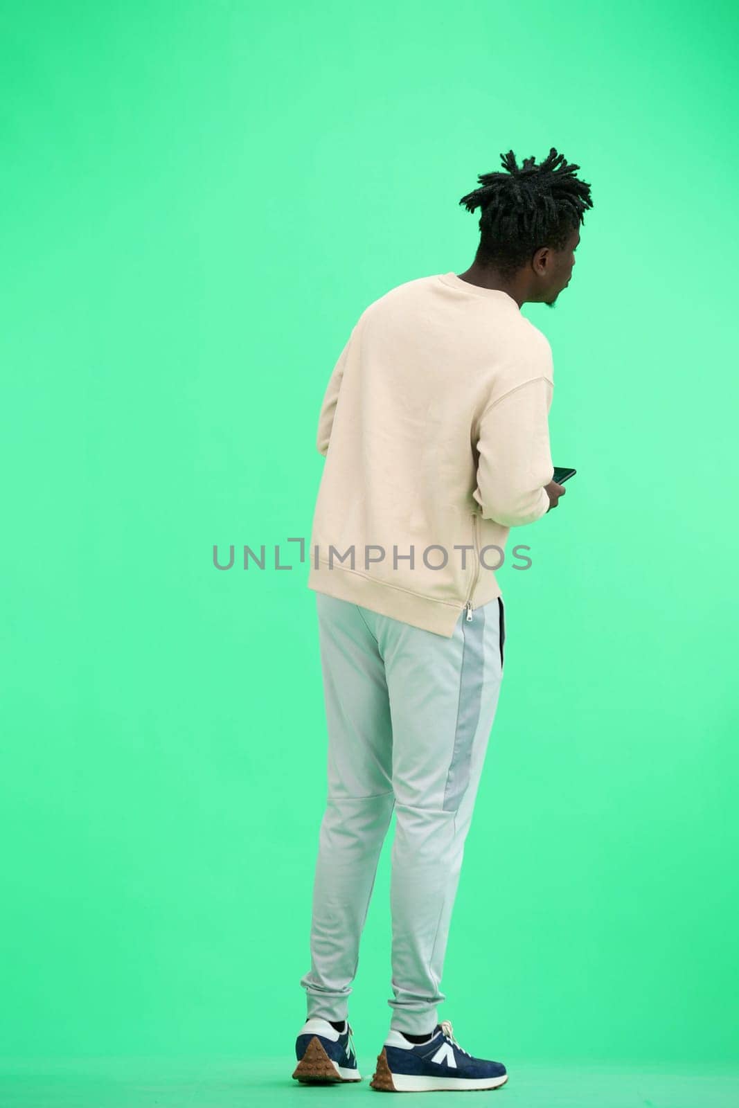 A man, full-length, on a green background, uses a phone.