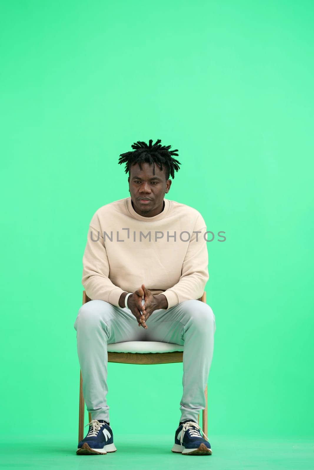 A man, on a green background, sitting on a chair.