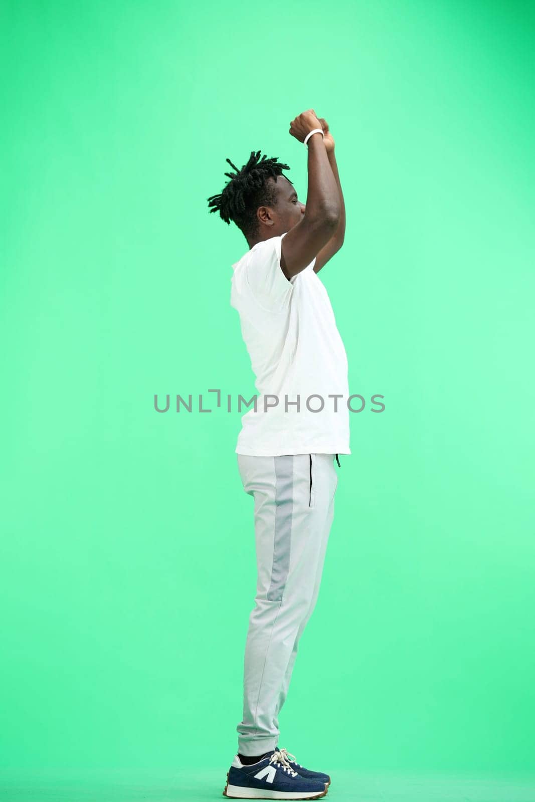 A man, full-length, on a green background, raised his hands.