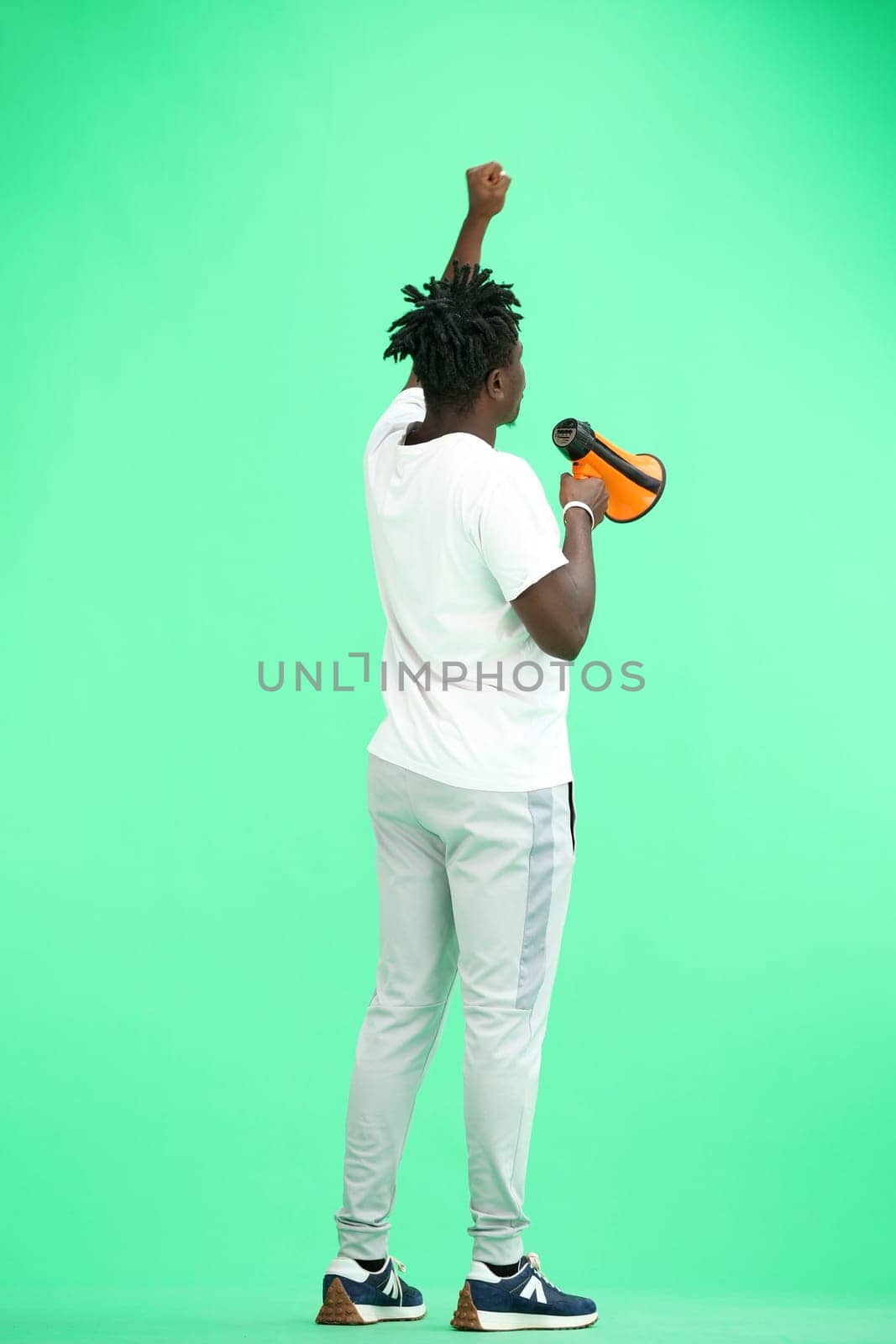 A man, full-length, on a green background, with a megaphone.
