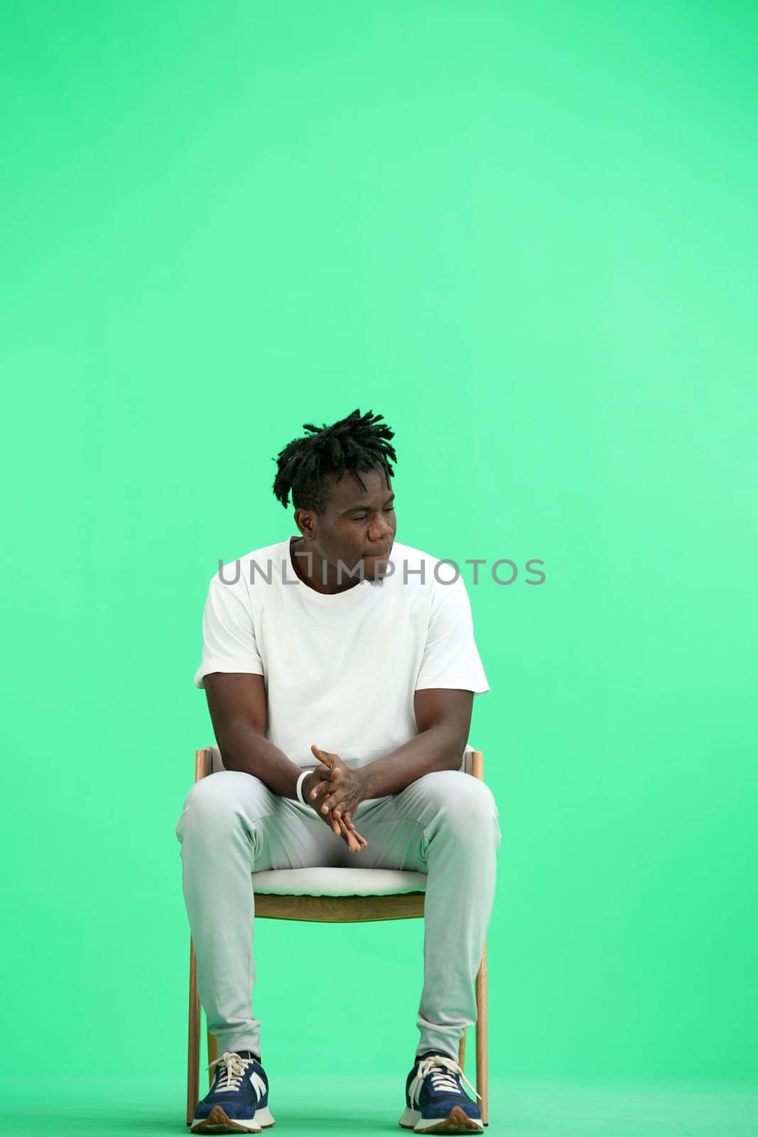 A man, on a green background, sitting on a chair.
