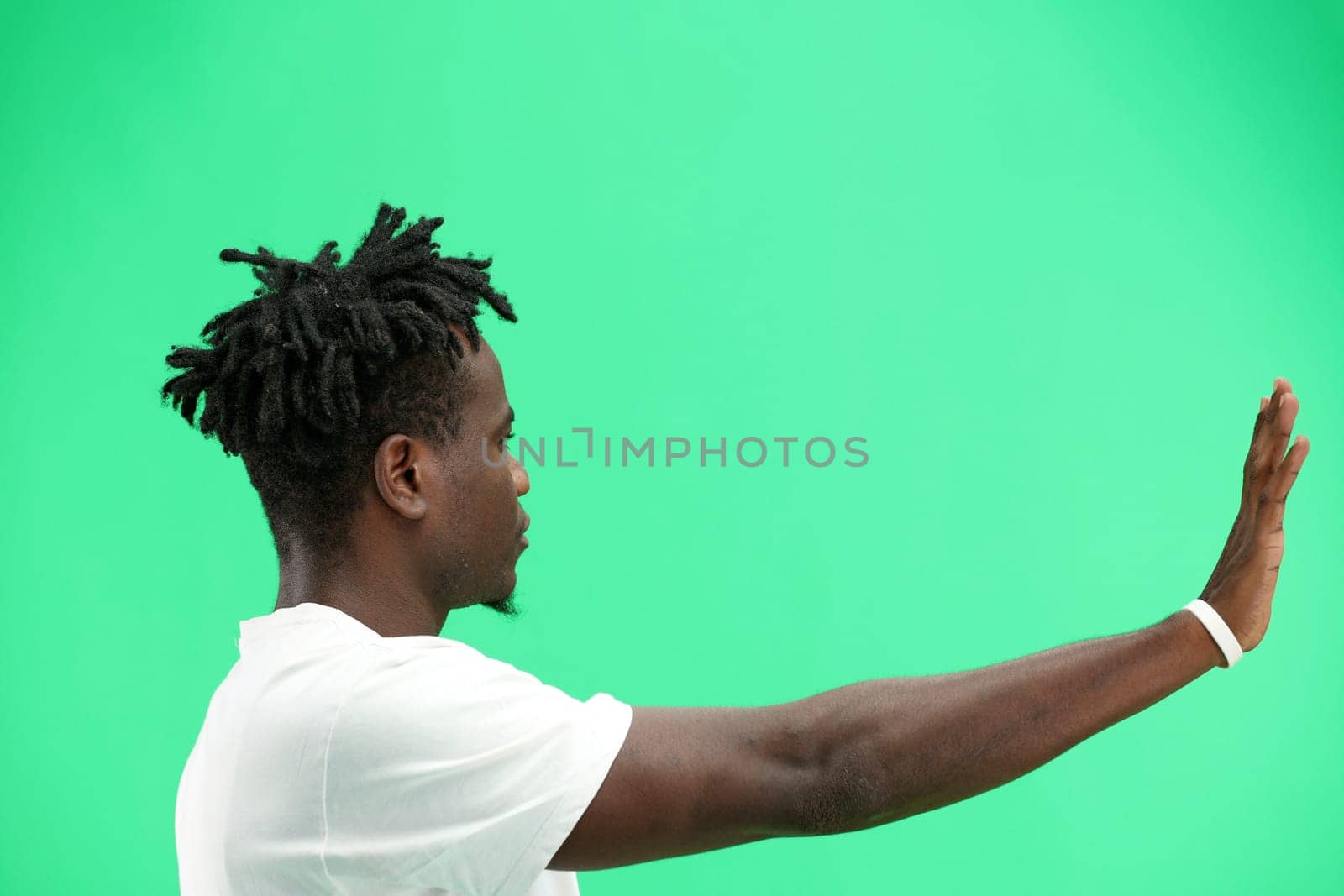 A man, close-up, on a green background, shows a stop sign.