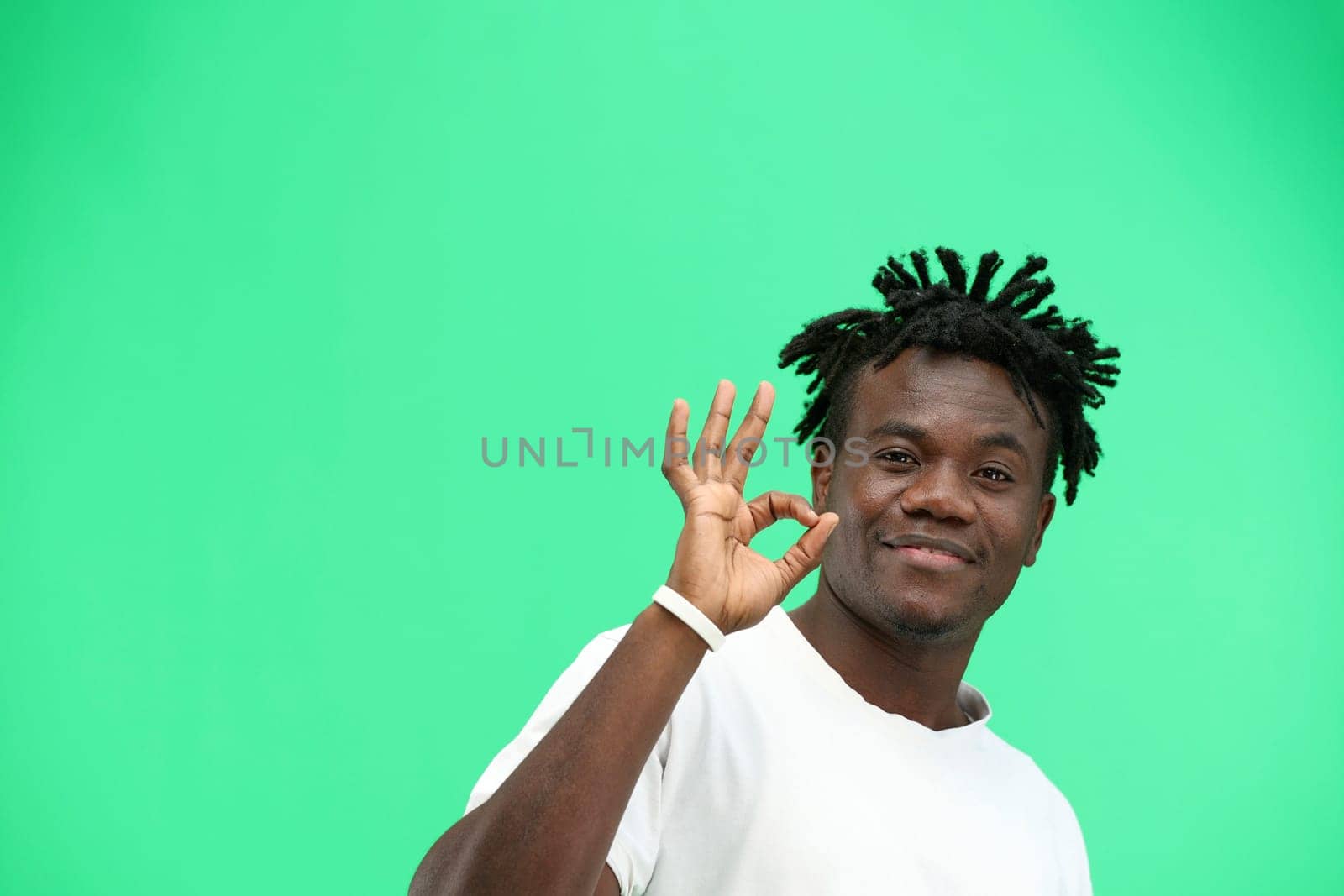 A man, close-up, on a green background, shows an ok sign.