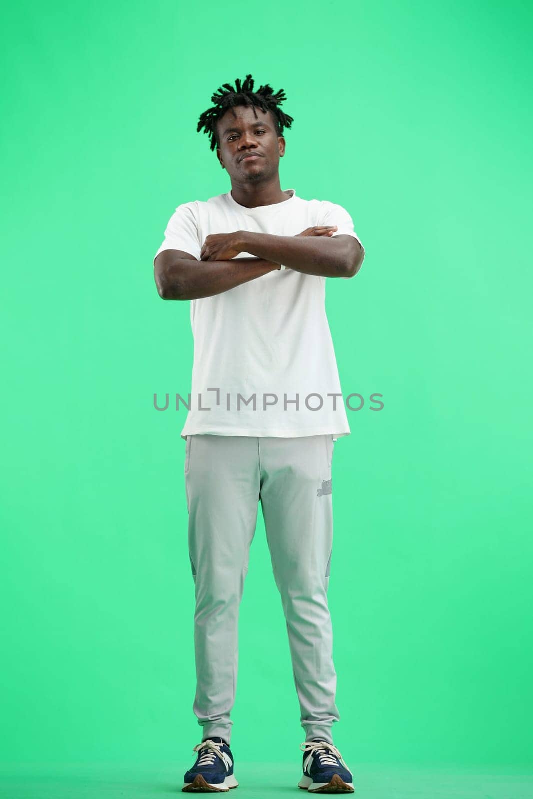 A man, full-length, on a green background, crossed his arms.