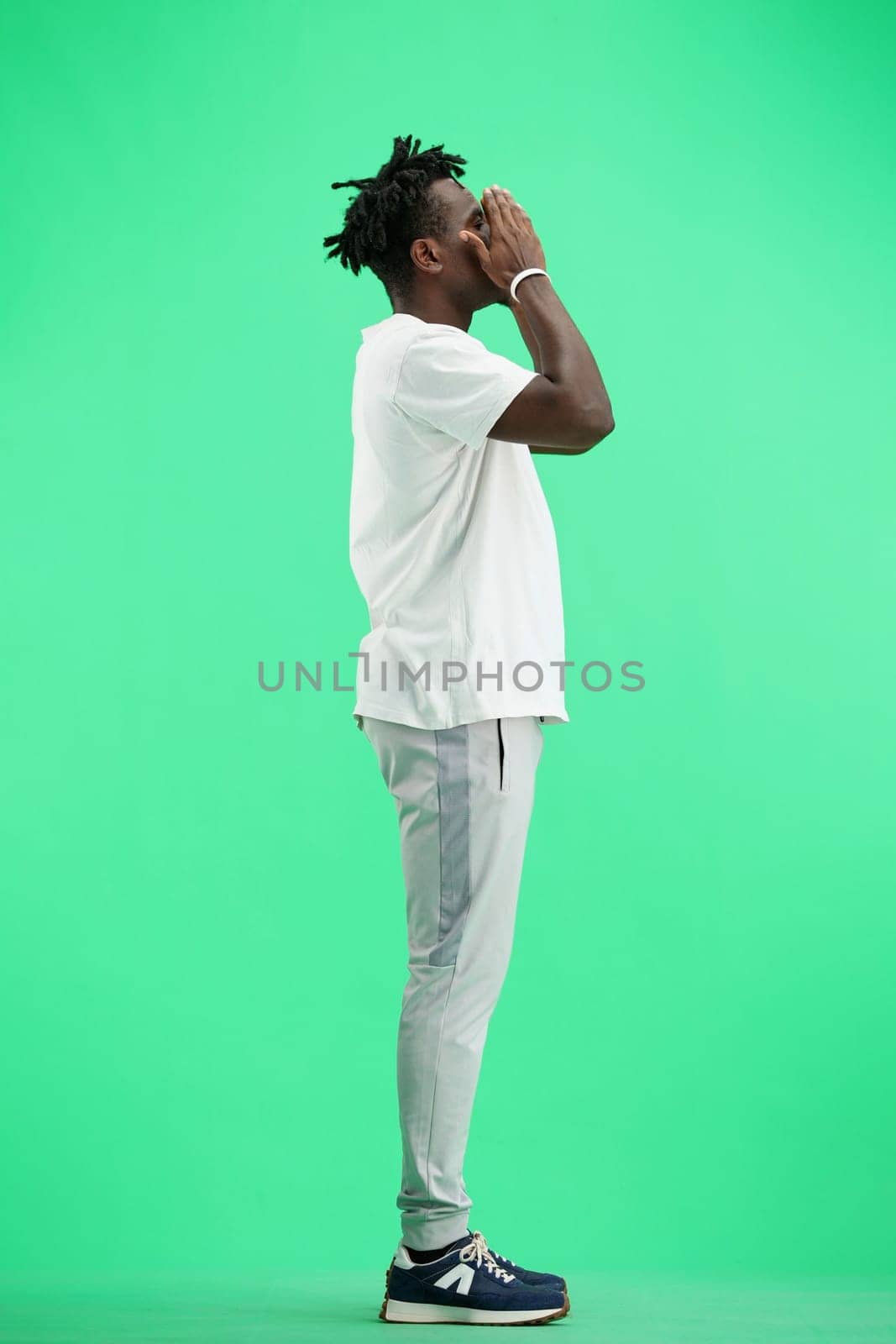 A man, full-length, on a green background, clutched his head.