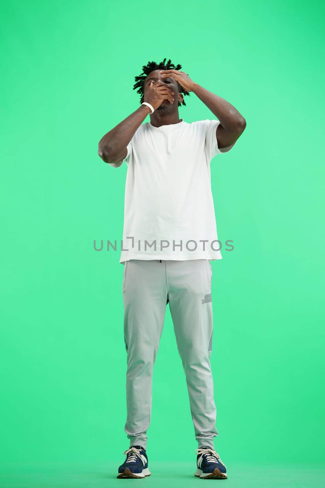 A man, full-length, on a green background, yawns.