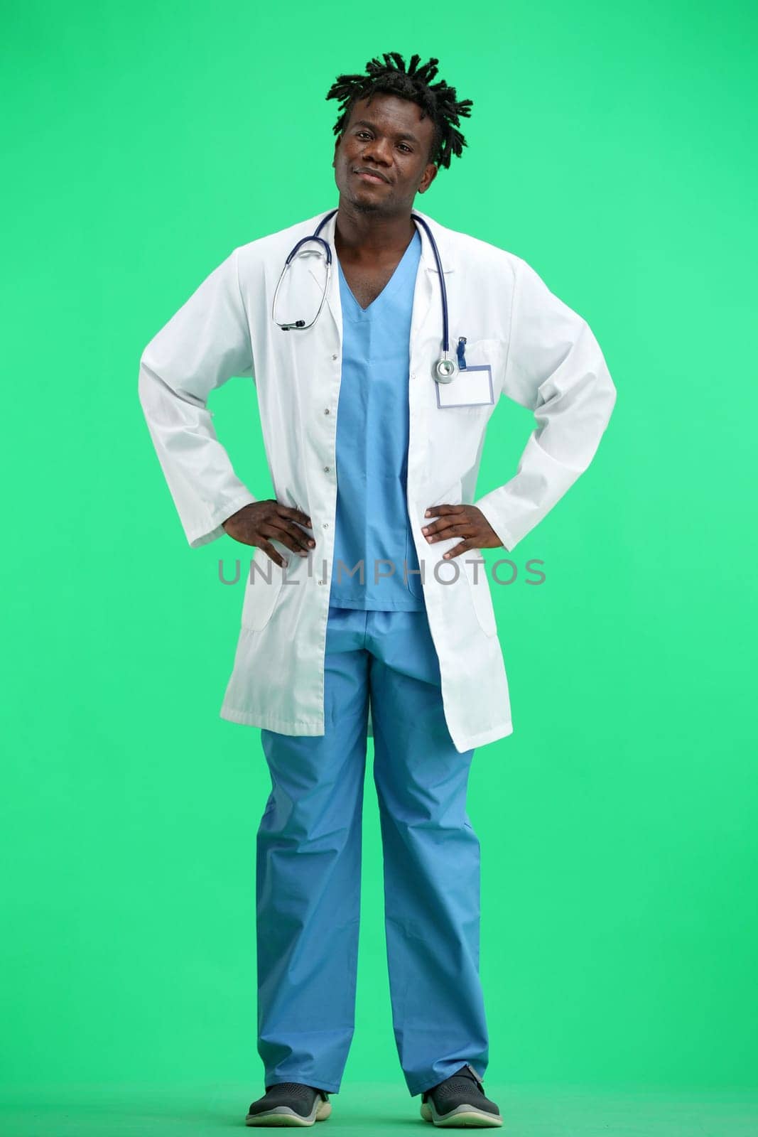 Doctor, full-length, on a green background, hands on hips.