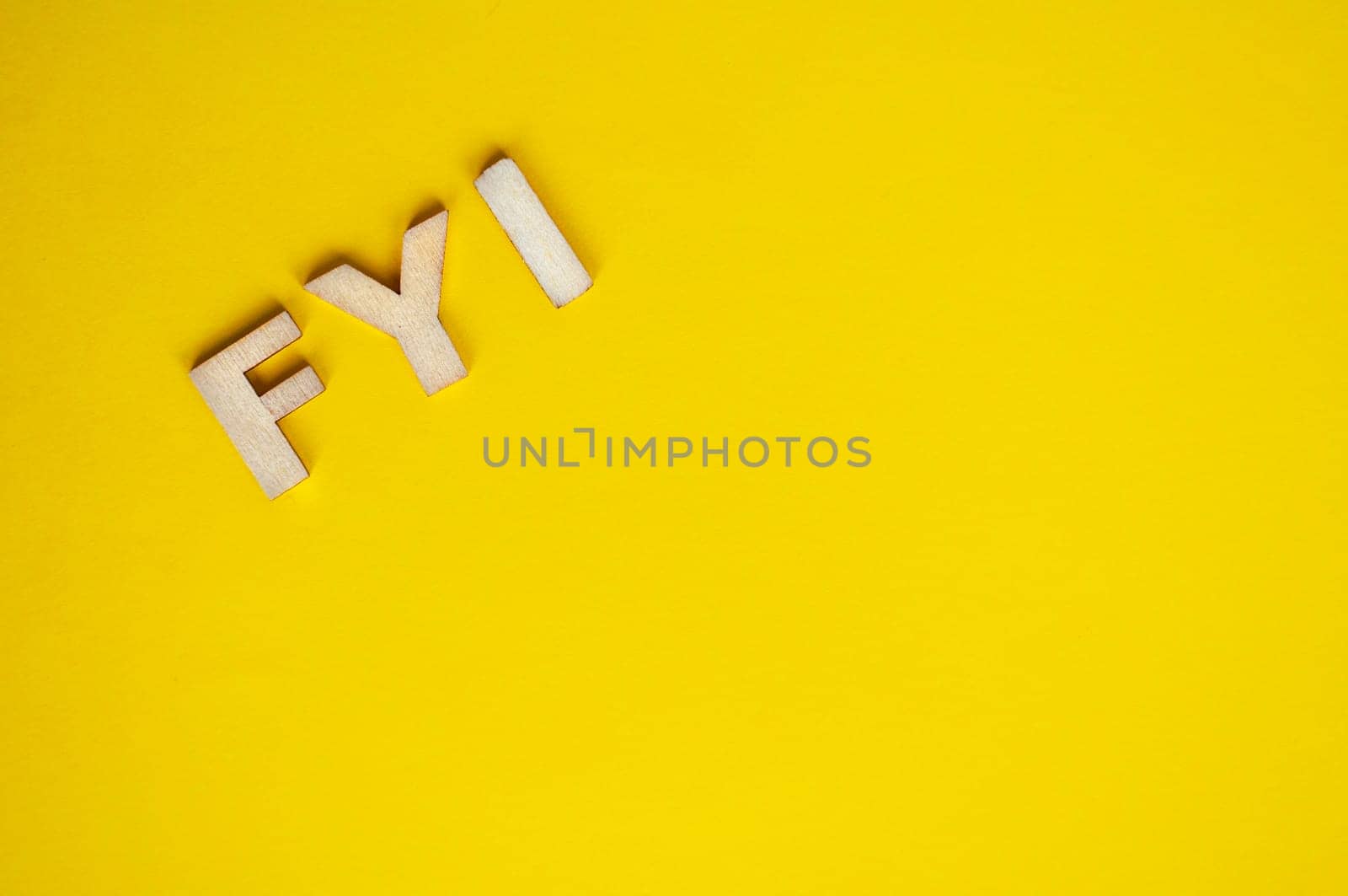 Top view of wooden FYI text on yellow background with customizable space for text.