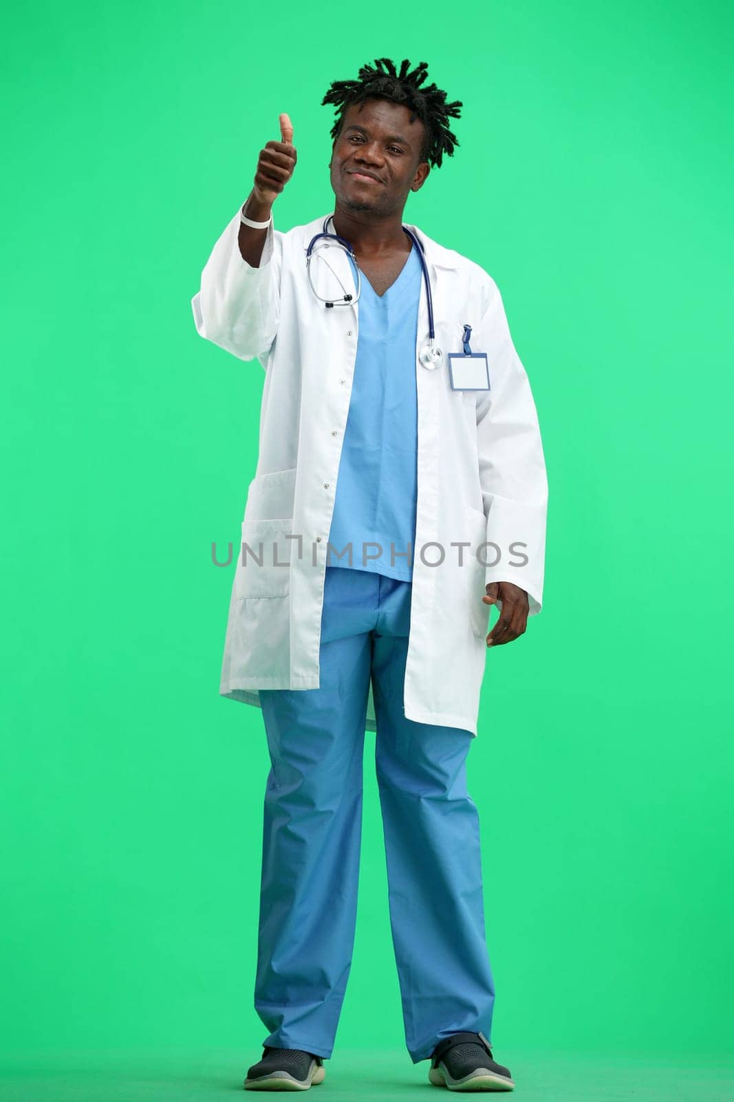 The doctor, in full height, on a green background, shows a thumbs up.