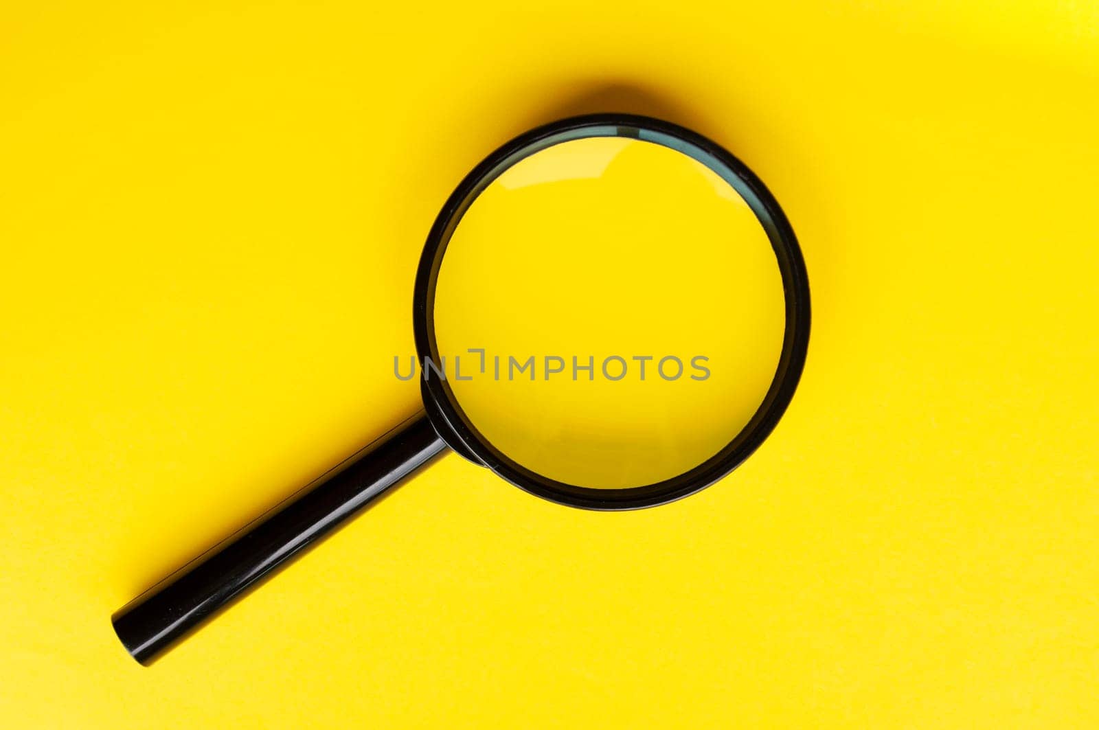 Top view of magnifying glass on yellow background with customizable space for text. Copy space.