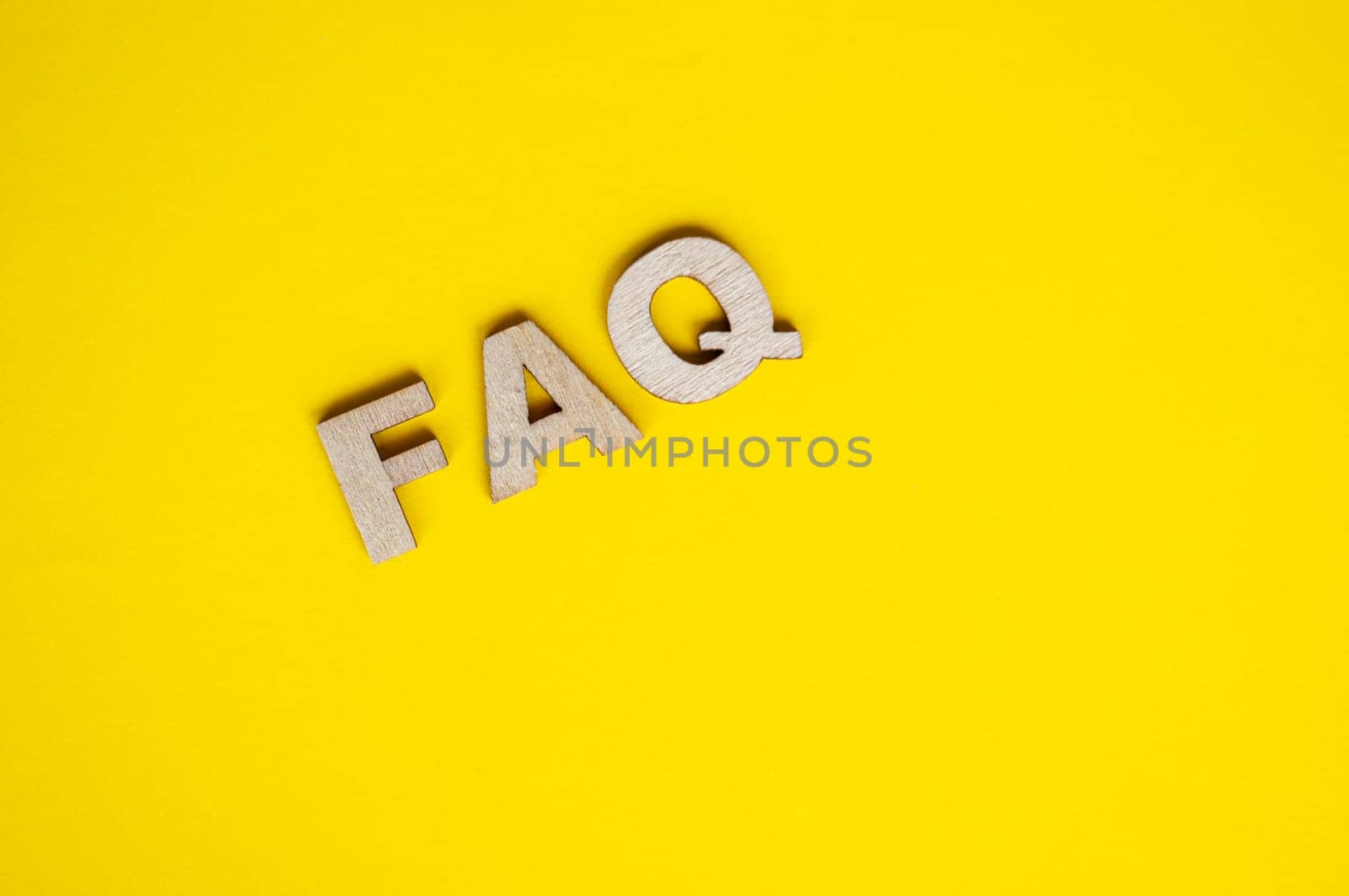 Top view of wooden FAQ text on yellow background. Frequently ask questions concept.