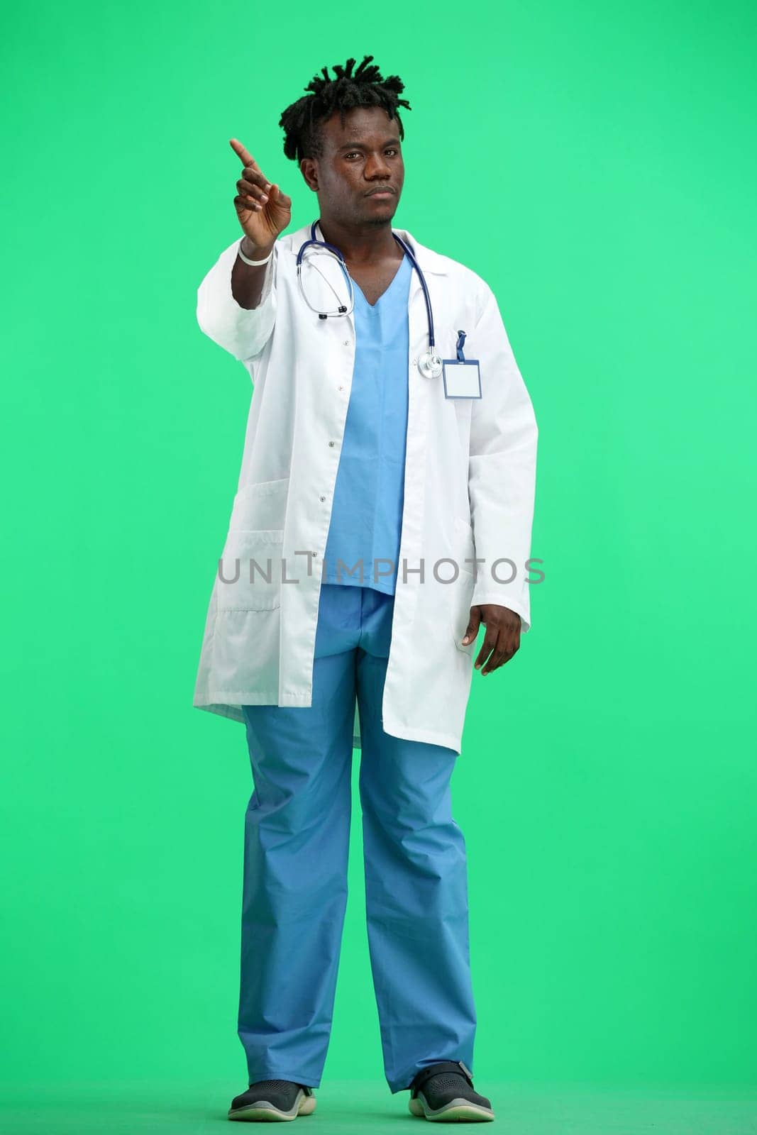 The doctor, in full height, on a green background, shows a forbidding sign.