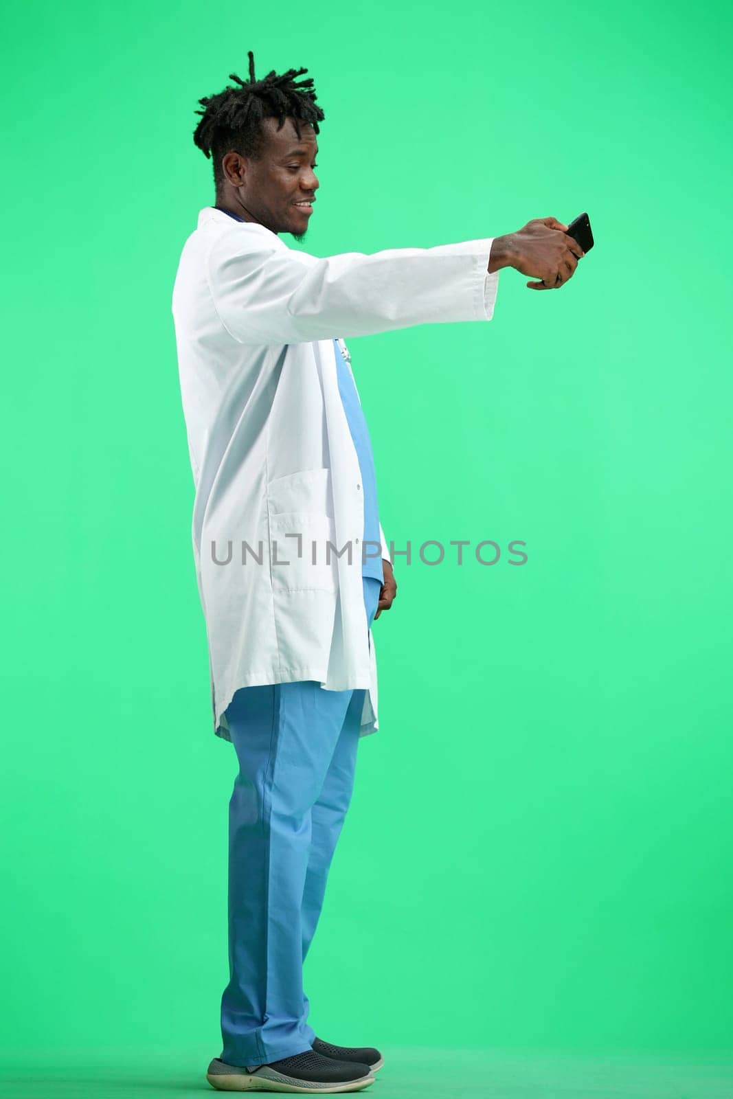 The doctor, in full height, on a green background, talking on the phone.