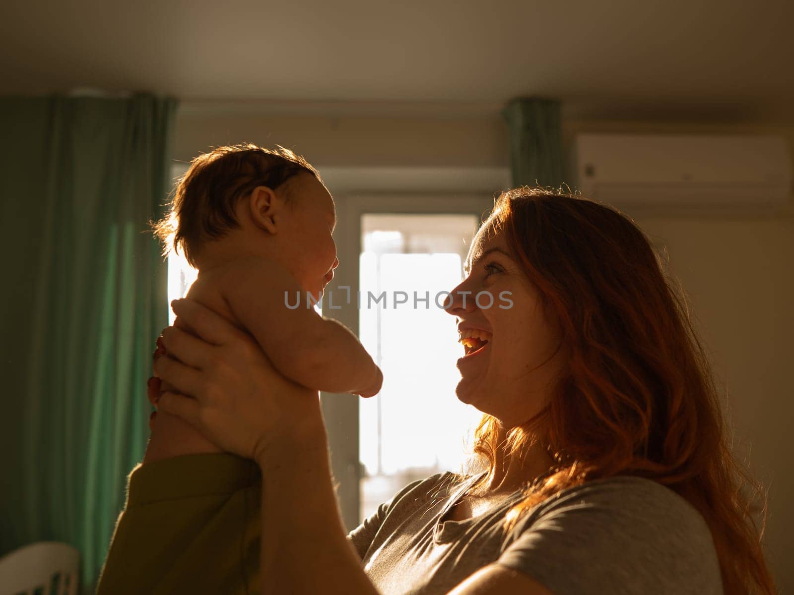 A Caucasian woman tenderly holds her newborn son in the morning rays of sunlight