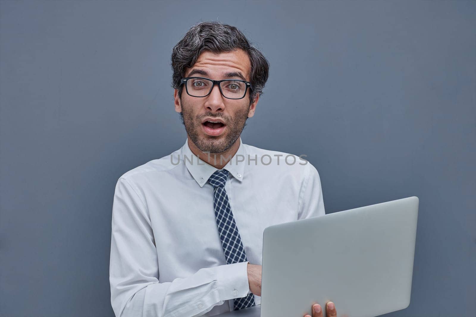 young successful man on a gray background typing in a laptop. surprised.
