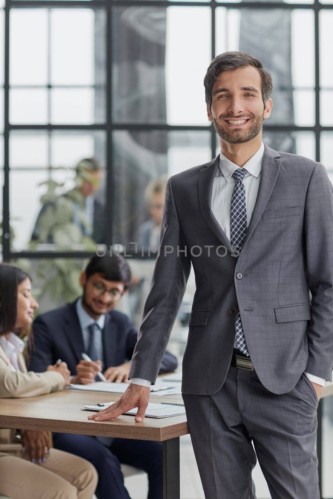 professional businessman, executive director of the company, sitting at the table in the office, with colleagues in the background
