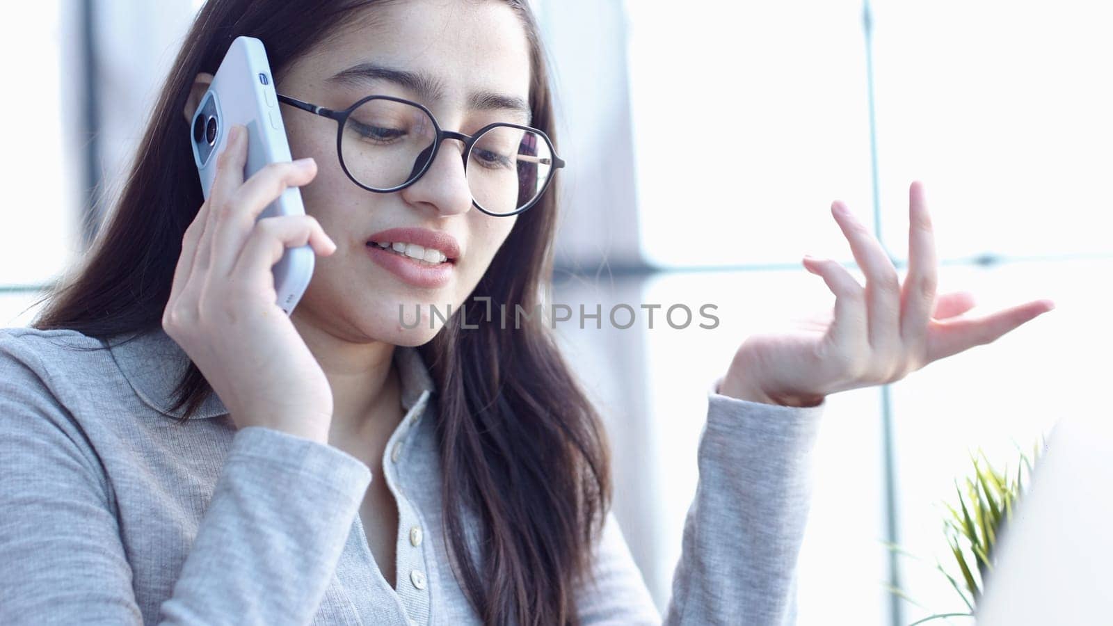 A young woman with glasses in the office talking on the phone.