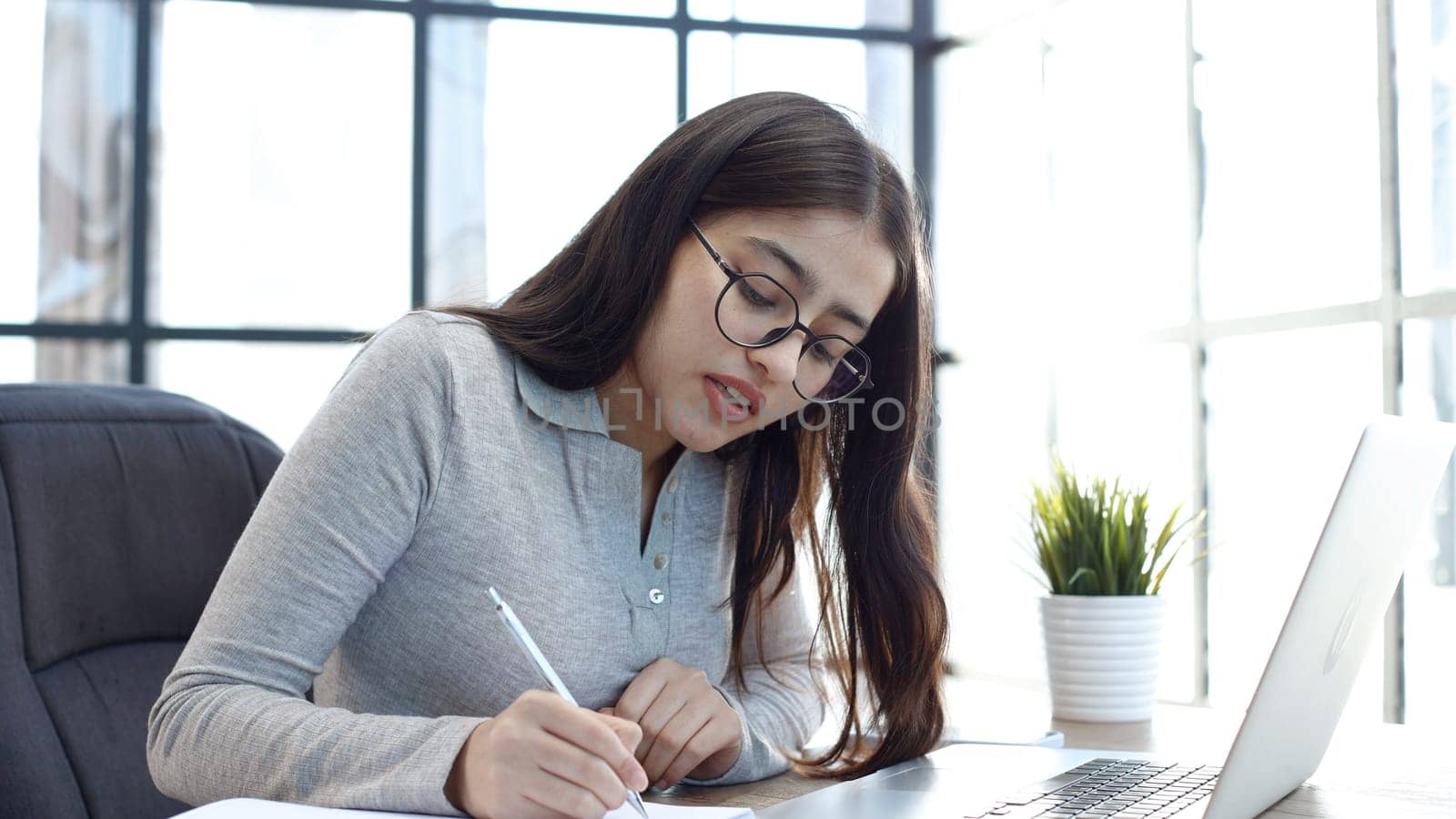 A young woman with glasses in the office is working on a laptop.