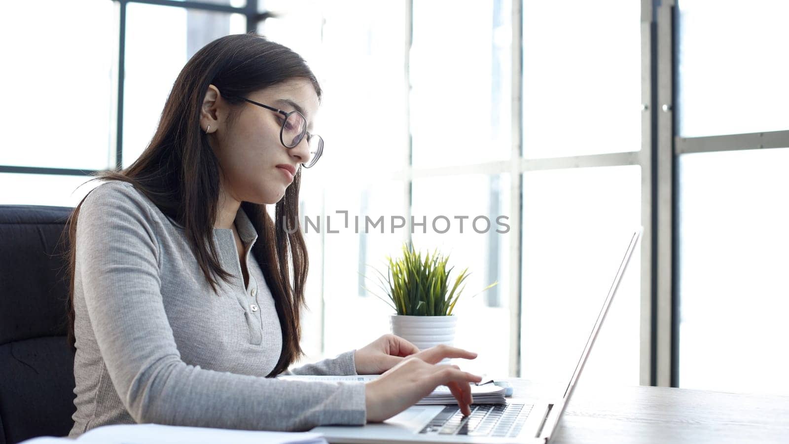 A young woman with glasses in the office is working with a laptop.